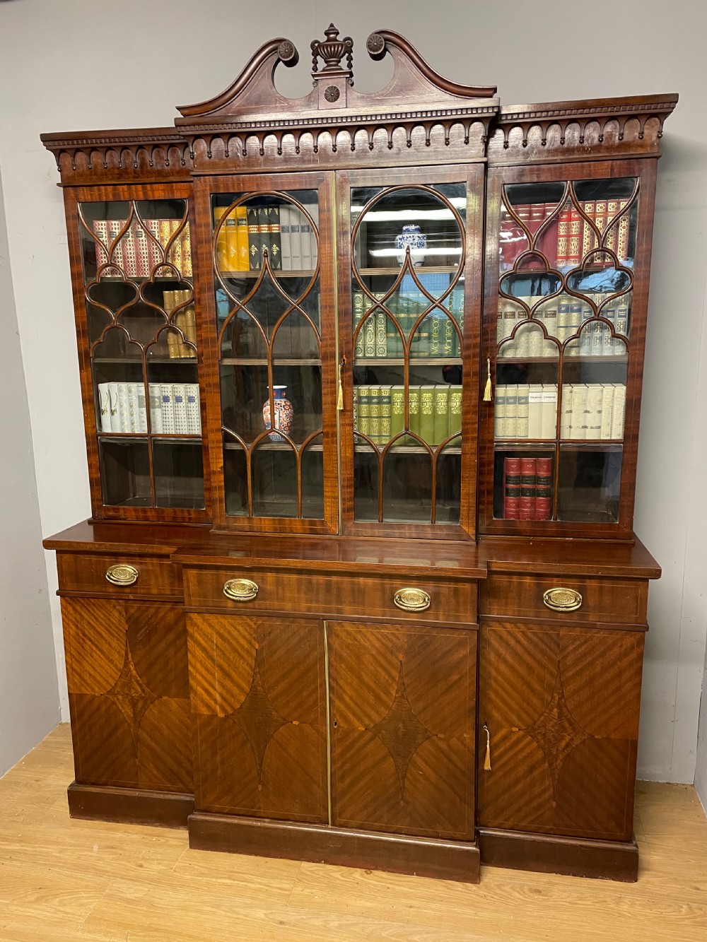 An Edwardian mahogany breakfront library bookcase with astragal glazed doors, a swan-neck pediment, and inlaid wood cabinet doors.