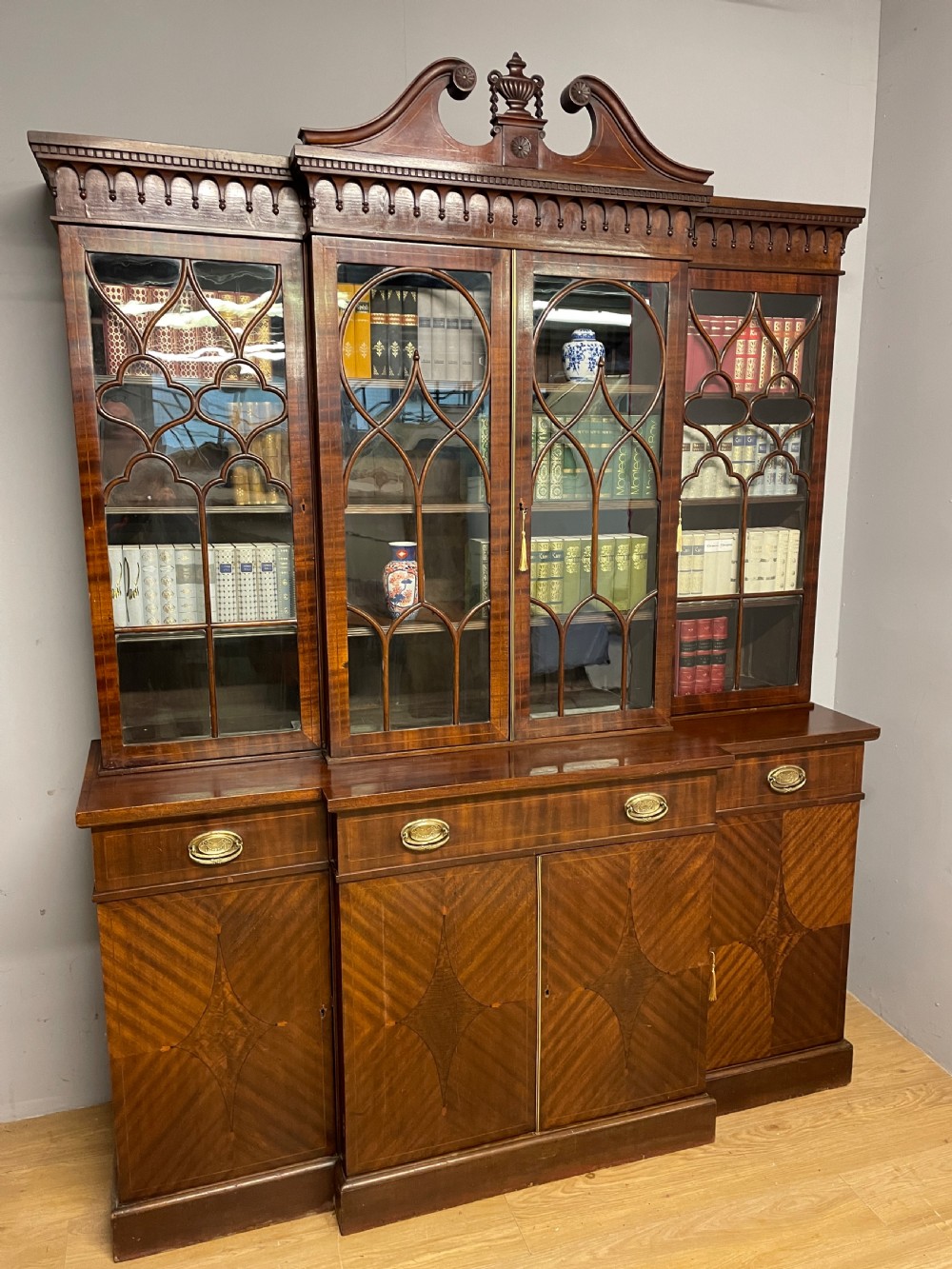 An Edwardian mahogany breakfront library bookcase with astragal glazed doors, a swan-neck pediment, and inlaid wood cabinet doors. View II