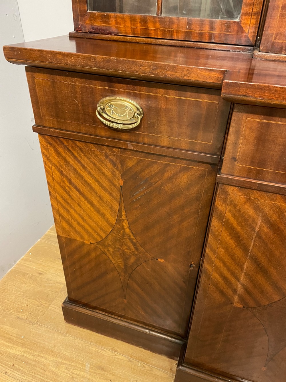 An Edwardian mahogany breakfront library bookcase with astragal glazed doors, a swan-neck pediment, and inlaid wood cabinet doors. View V