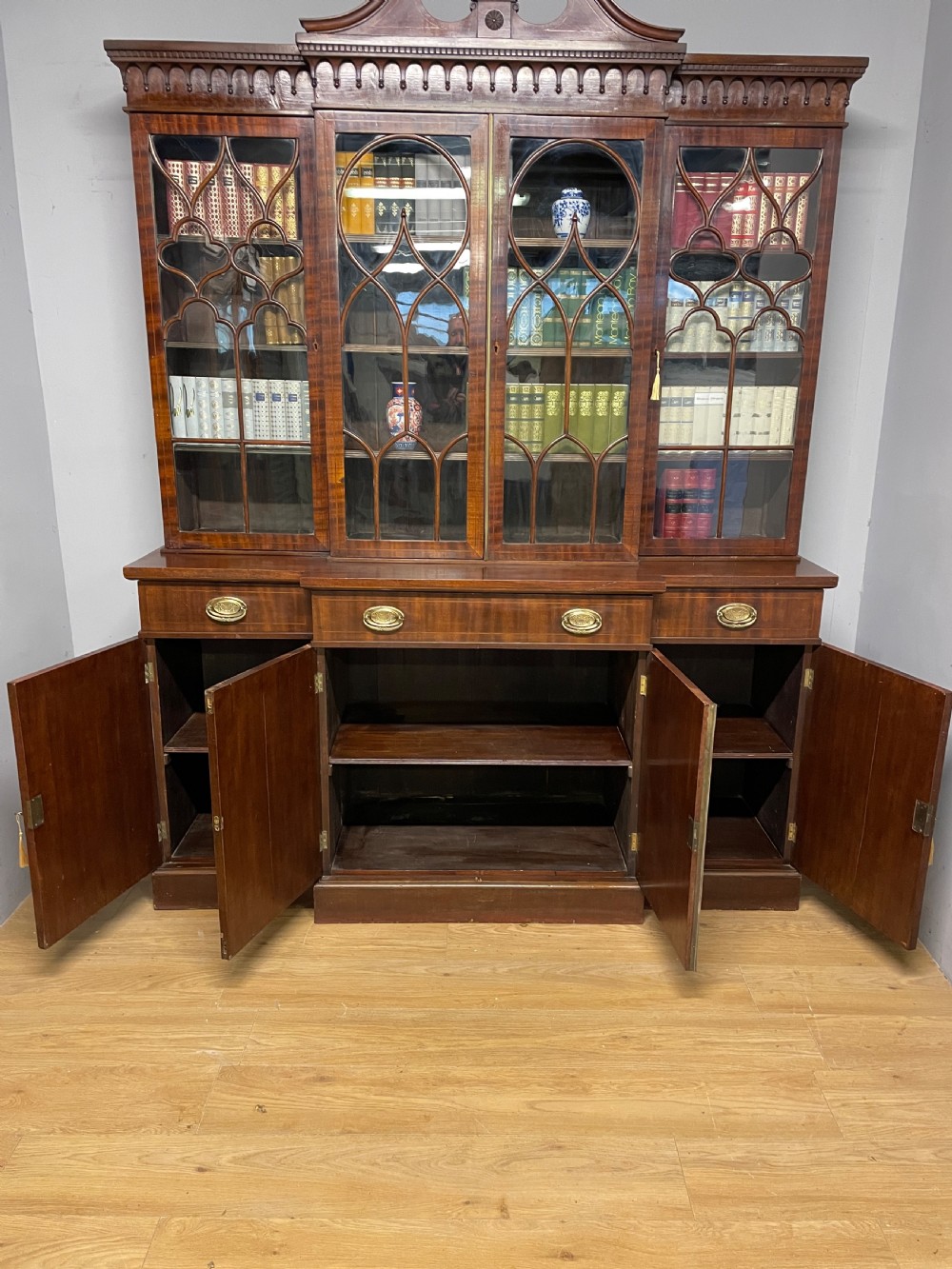 An Edwardian mahogany breakfront library bookcase with astragal glazed doors, a swan-neck pediment, and inlaid wood cabinet doors. View VIII