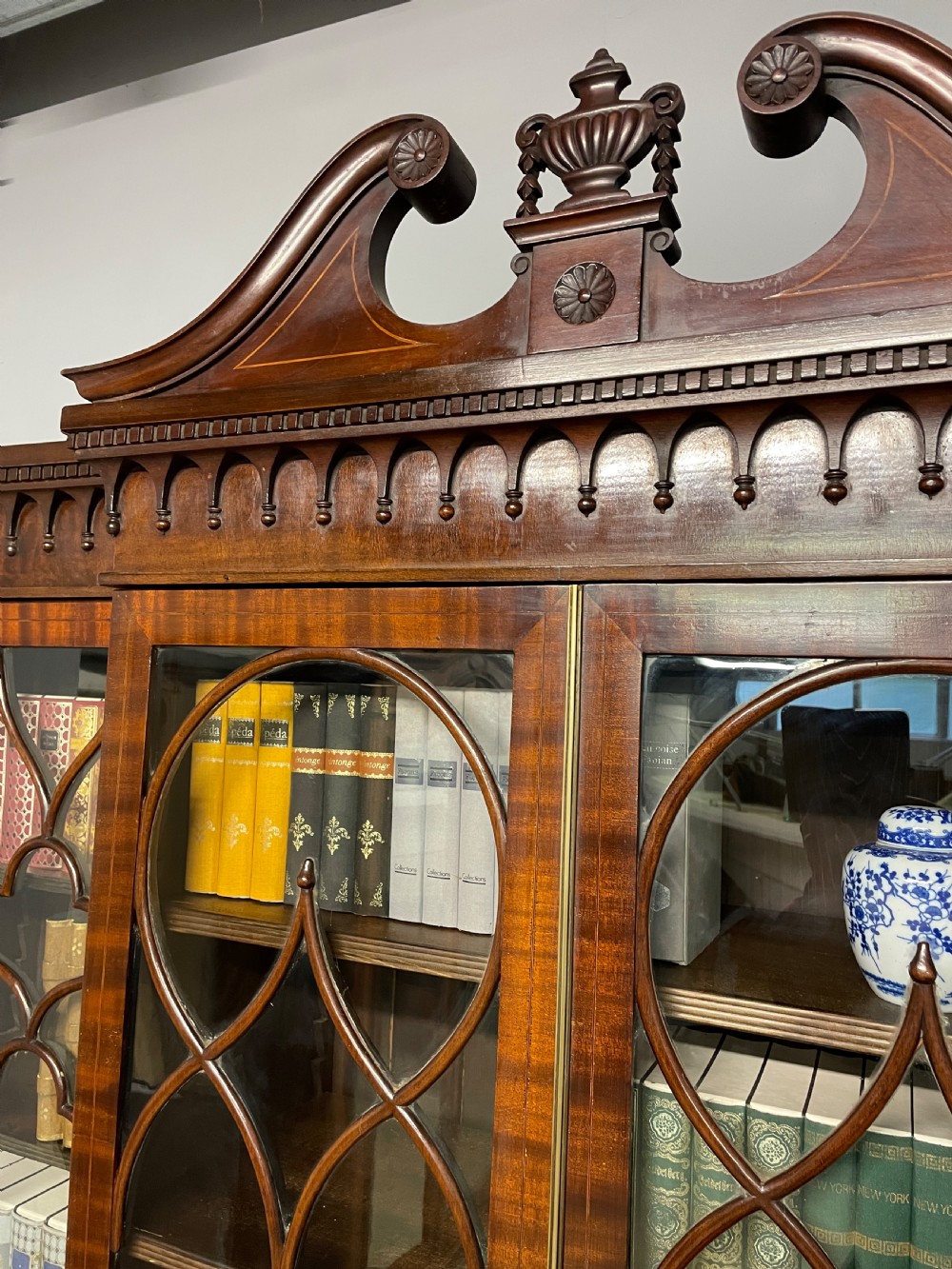An Edwardian mahogany breakfront library bookcase with astragal glazed doors, a swan-neck pediment, and inlaid wood cabinet doors. View IX