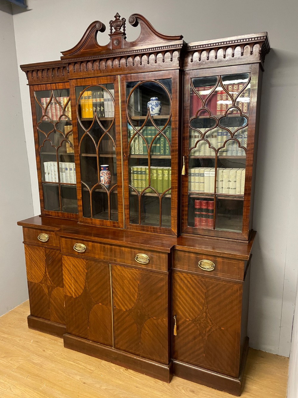 An Edwardian mahogany breakfront library bookcase with astragal glazed doors, a swan-neck pediment, and inlaid wood cabinet doors. View XII