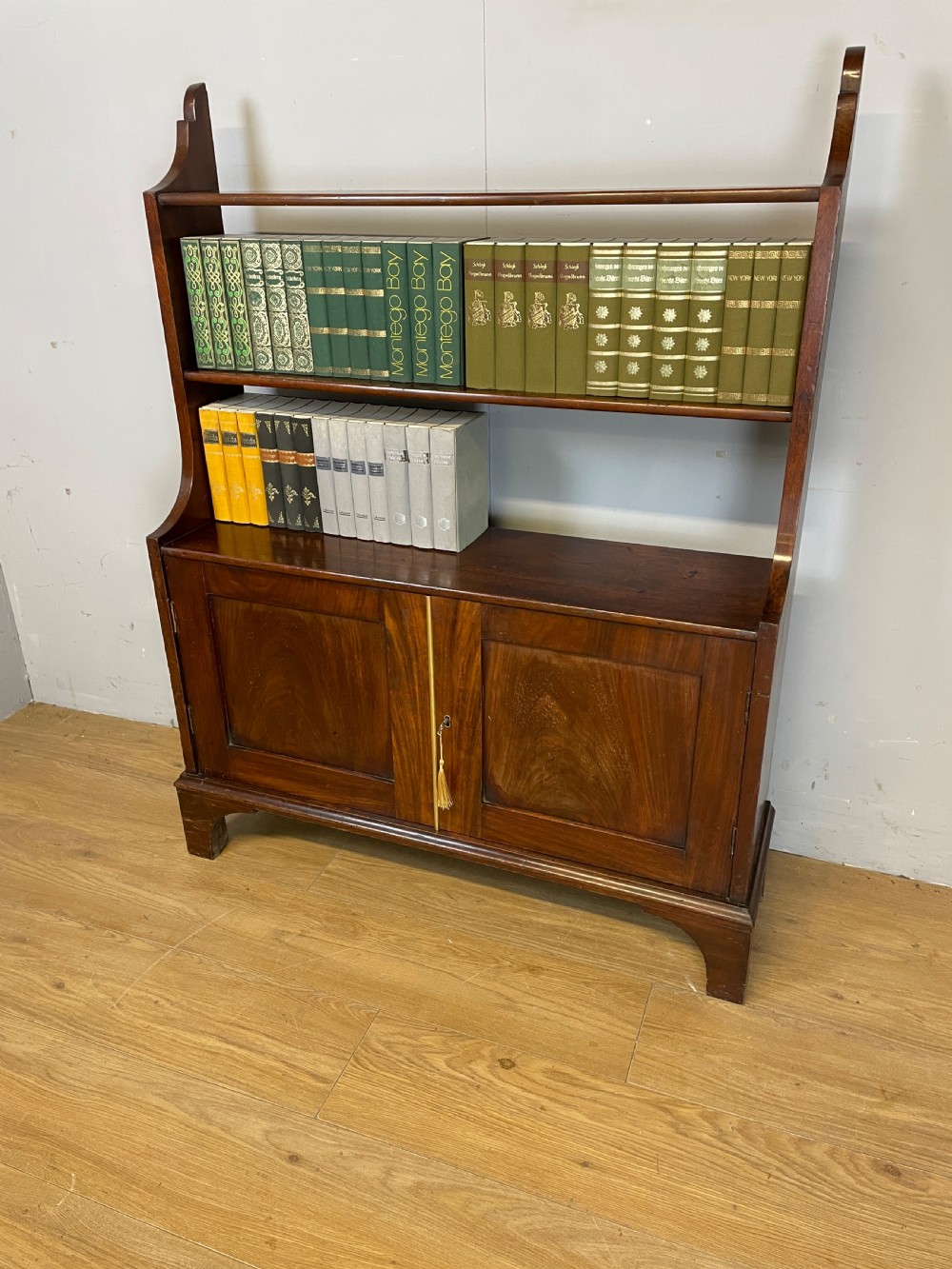 A 19th-century flame mahogany waterfall freestanding bookcase featuring graduated open shelves above a two-door lower cupboard with bracket feet.