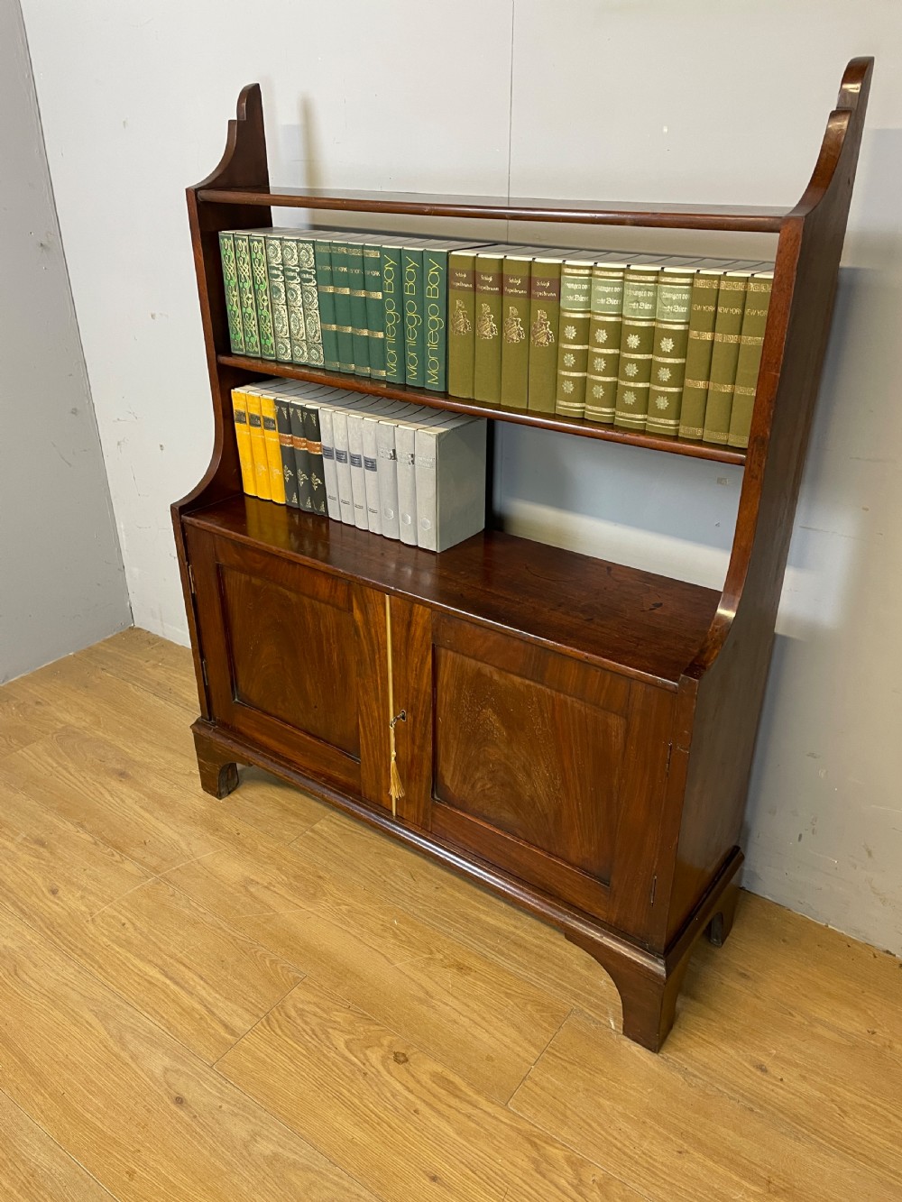 A 19th-century flame mahogany waterfall freestanding bookcase featuring graduated open shelves above a two-door lower cupboard with bracket feet. View II