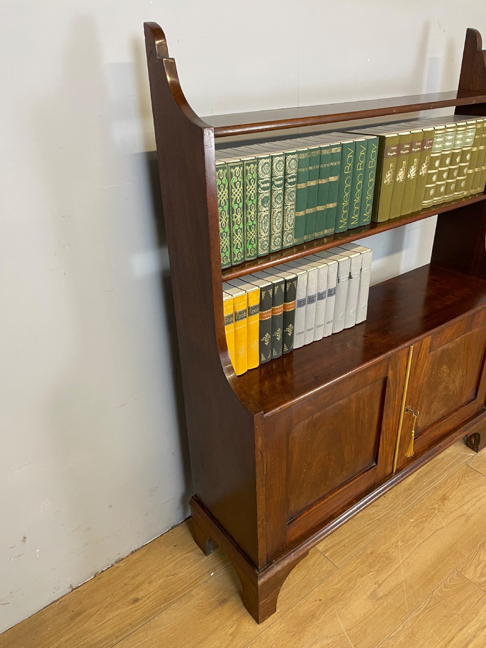 A 19th-century flame mahogany waterfall freestanding bookcase featuring graduated open shelves above a two-door lower cupboard with bracket feet. View IV