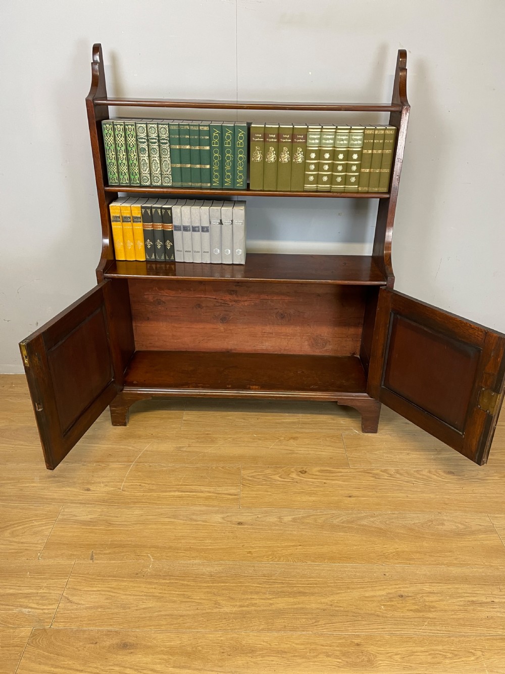 A 19th-century flame mahogany waterfall freestanding bookcase featuring graduated open shelves above a two-door lower cupboard with bracket feet. View VI