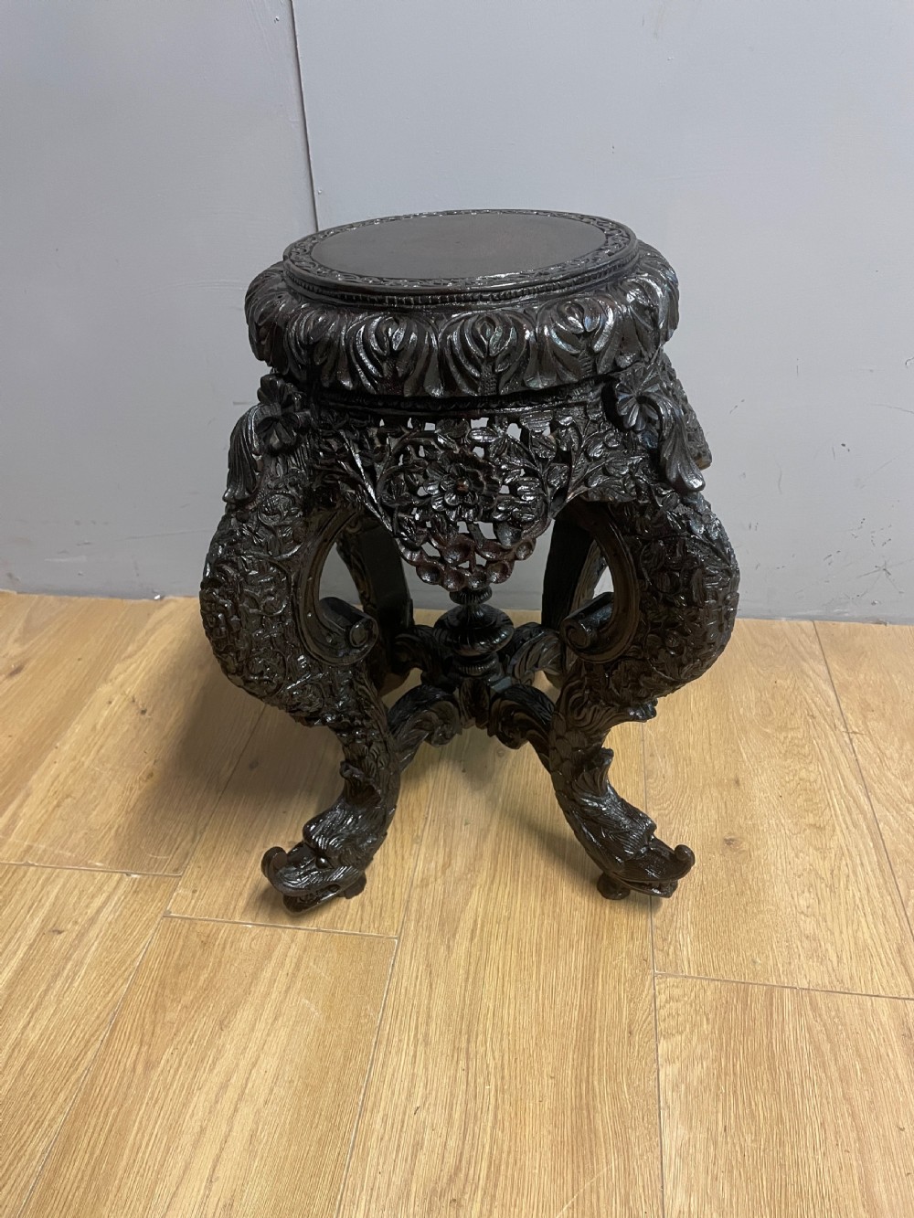 A dark circular carved hardwood stand with pierced foliate aprons and heavy curved legs with detailed carved feet.