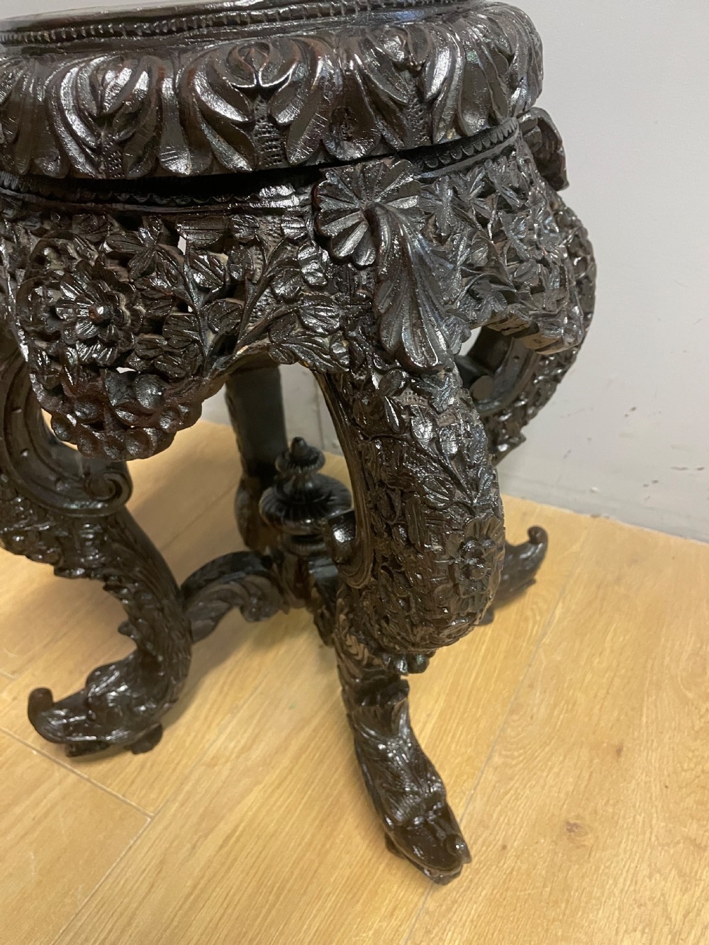 A dark circular carved hardwood stand with pierced foliate aprons and heavy curved legs with detailed carved feet. View II