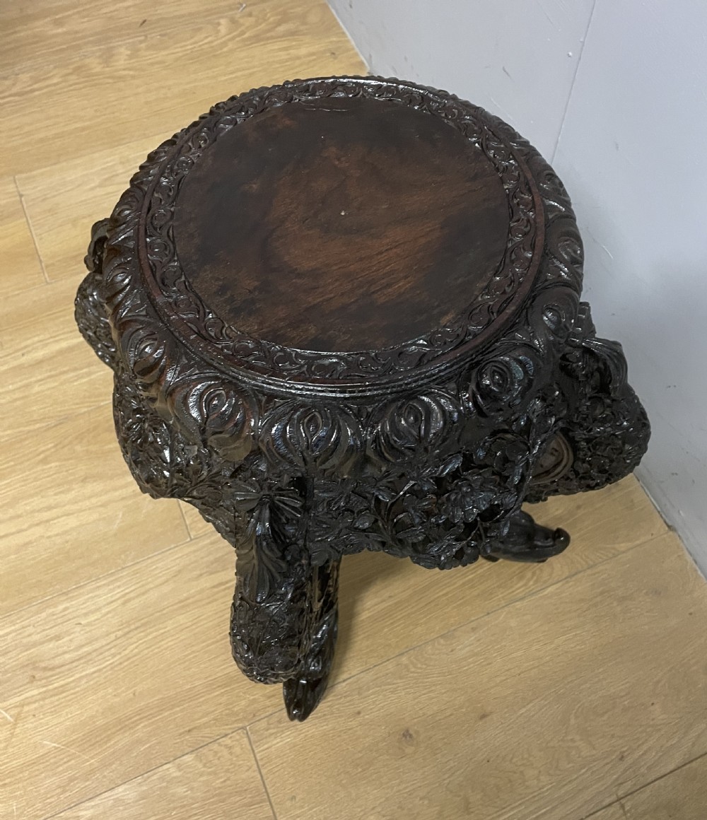 A dark circular carved hardwood stand with pierced foliate aprons and heavy curved legs with detailed carved feet. View V