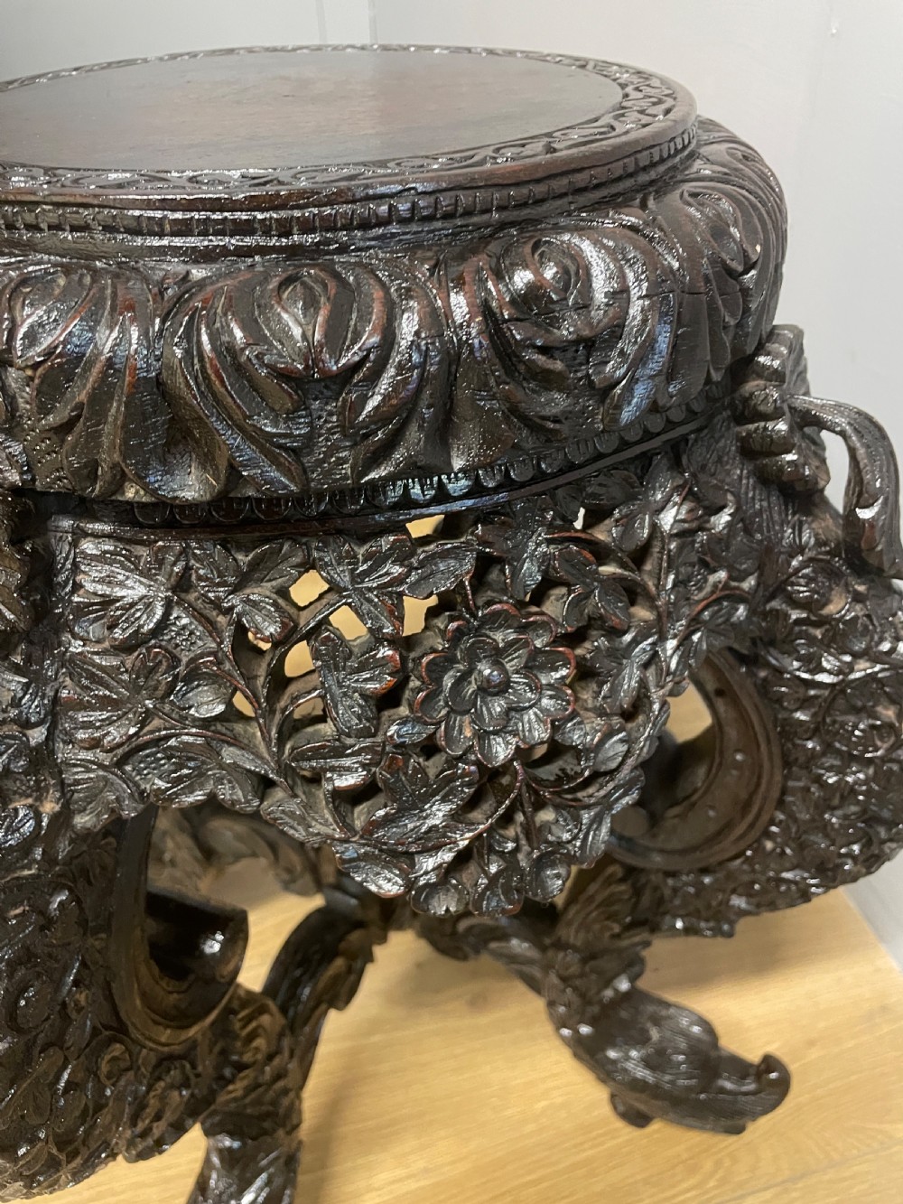 A dark circular carved hardwood stand with pierced foliate aprons and heavy curved legs with detailed carved feet. View VI