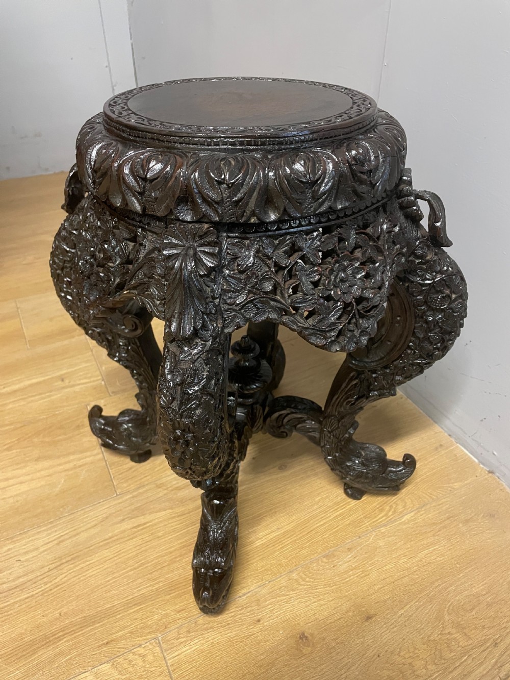 A dark circular carved hardwood stand with pierced foliate aprons and heavy curved legs with detailed carved feet. View VII