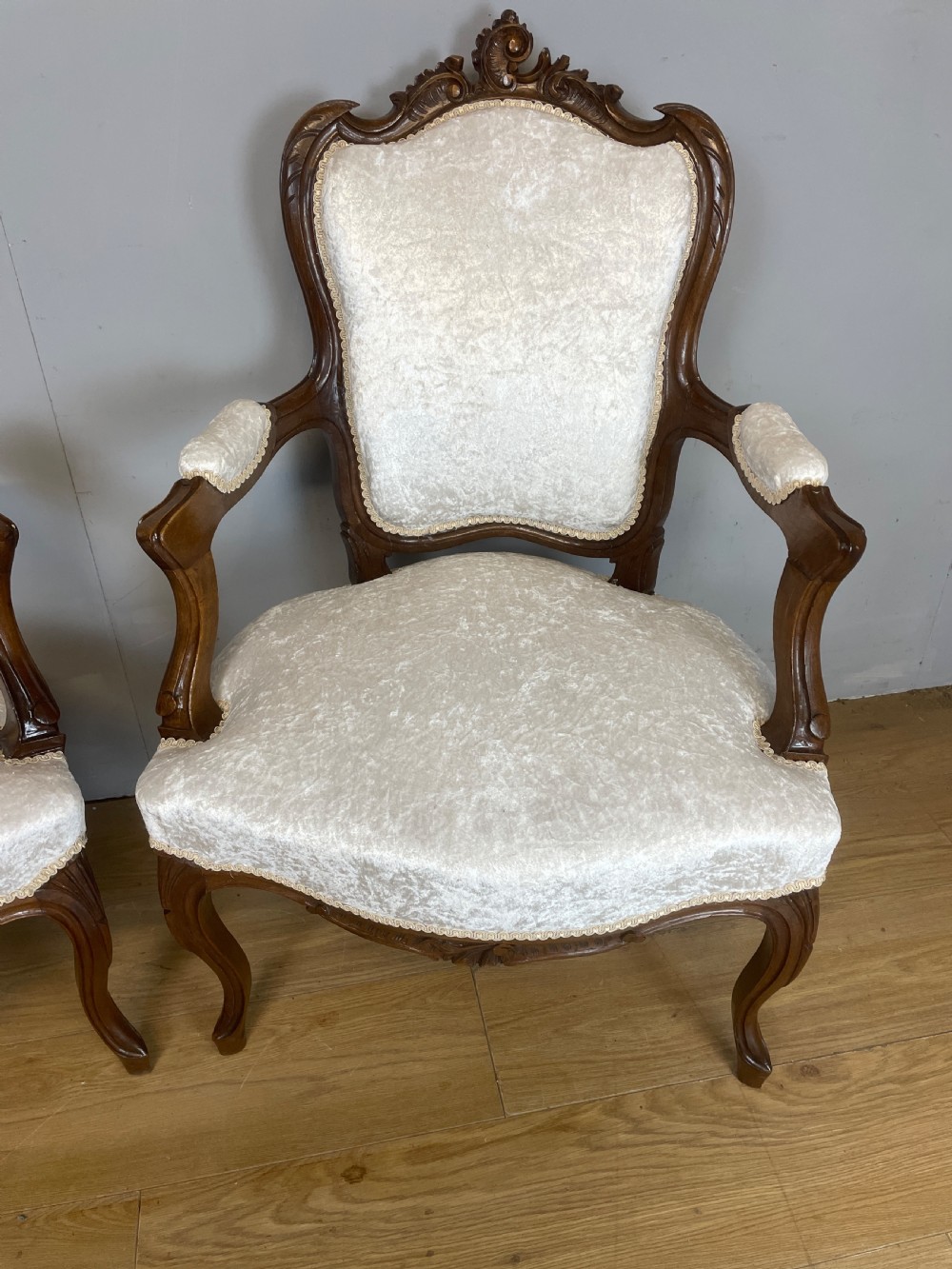 A pair of French carved walnut open armchairs upholstered in cream crushed fabric with cabriole legs and ornate cresting. View II