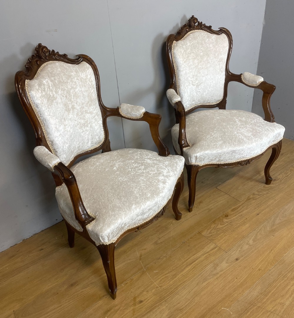 A pair of French carved walnut open armchairs upholstered in cream crushed fabric with cabriole legs and ornate cresting. View III