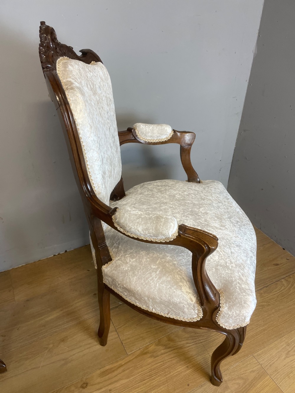 A pair of French carved walnut open armchairs upholstered in cream crushed fabric with cabriole legs and ornate cresting. View VIII