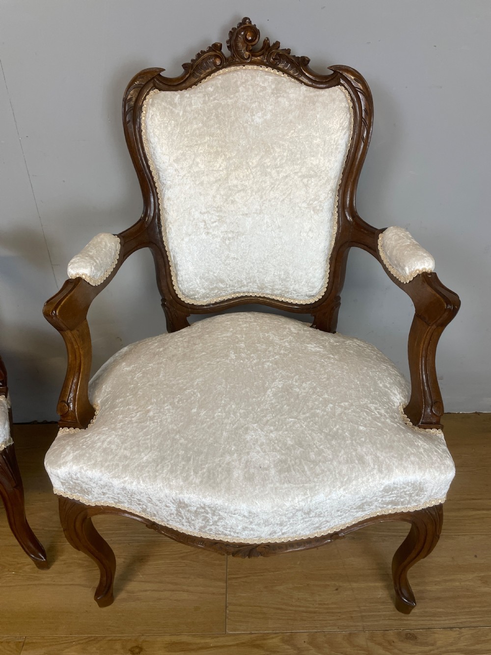 A pair of French carved walnut open armchairs upholstered in cream crushed fabric with cabriole legs and ornate cresting. View XI