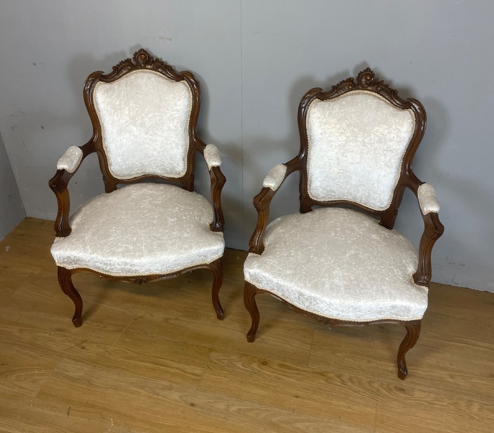 A pair of French carved walnut open armchairs upholstered in cream crushed fabric with cabriole legs and ornate cresting. View XII