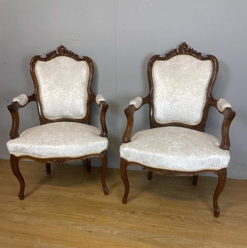 A pair of French carved walnut open armchairs upholstered in cream crushed fabric with cabriole legs and ornate cresting. View XIII