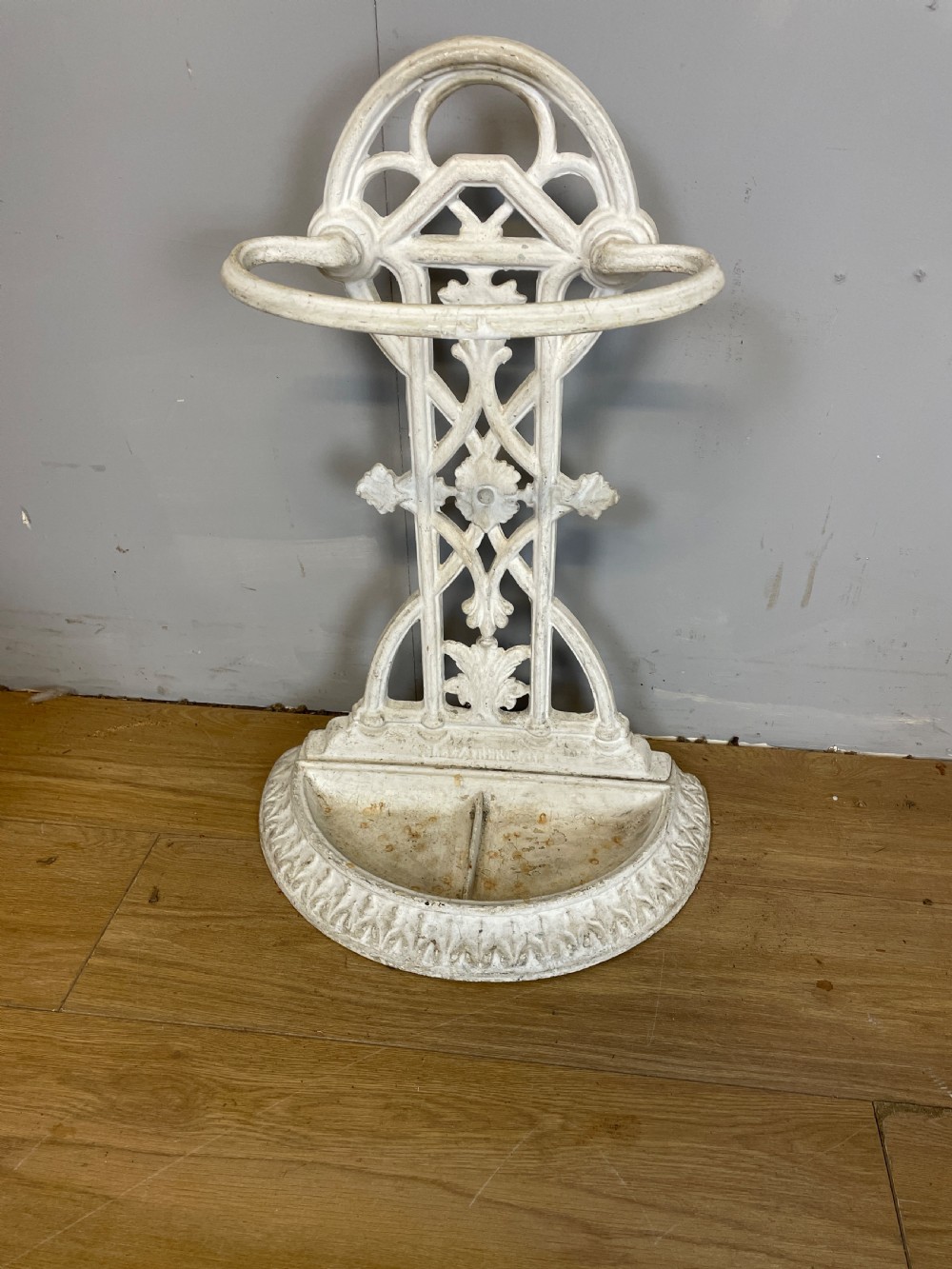 A white painted 19th-century Victorian cast iron stick stand featuring intricate Gothic tracery, an upper retaining hoop, and a divided drip tray base.