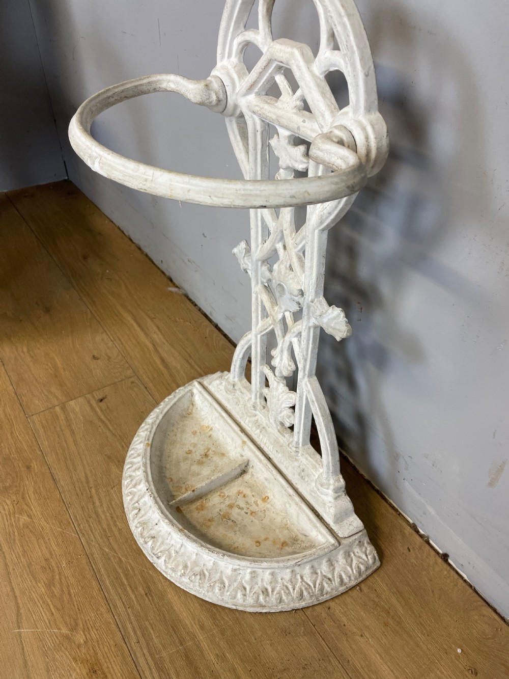 A white painted 19th-century Victorian cast iron stick stand featuring intricate Gothic tracery, an upper retaining hoop, and a divided drip tray base. View V
