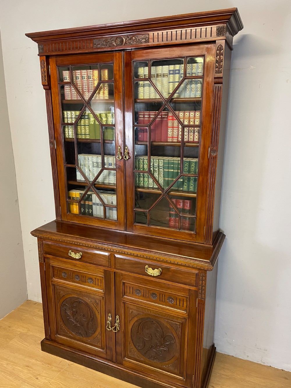 A late 19th-century solid walnut Arts and Crafts bookcase over cupboard featuring upper geometric astragal glazed doors and lower carved foliate panels.