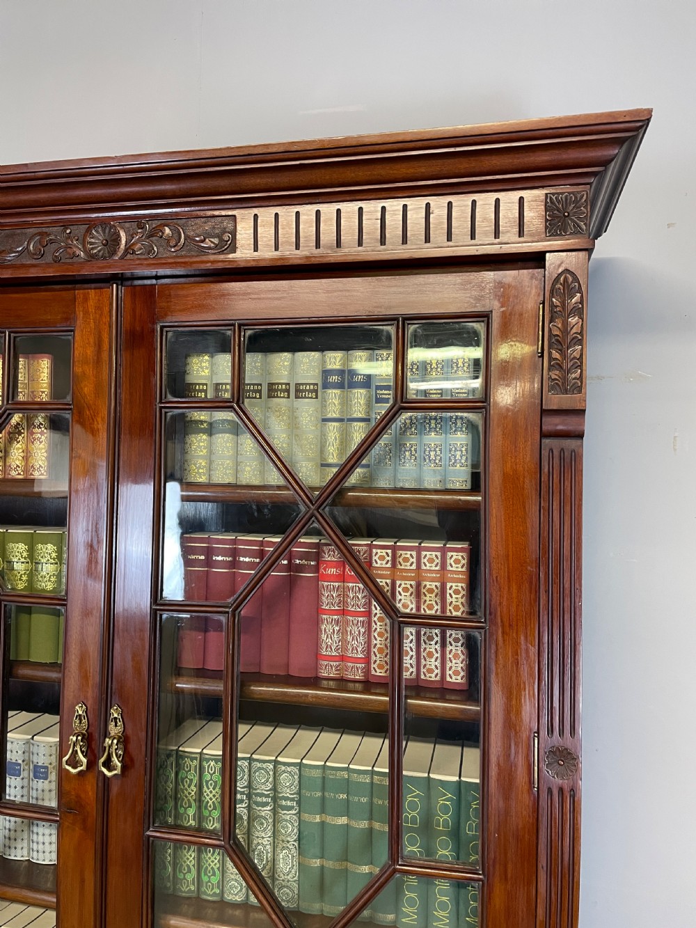 A late 19th-century solid walnut Arts and Crafts bookcase over cupboard featuring upper geometric astragal glazed doors and lower carved foliate panels. View III