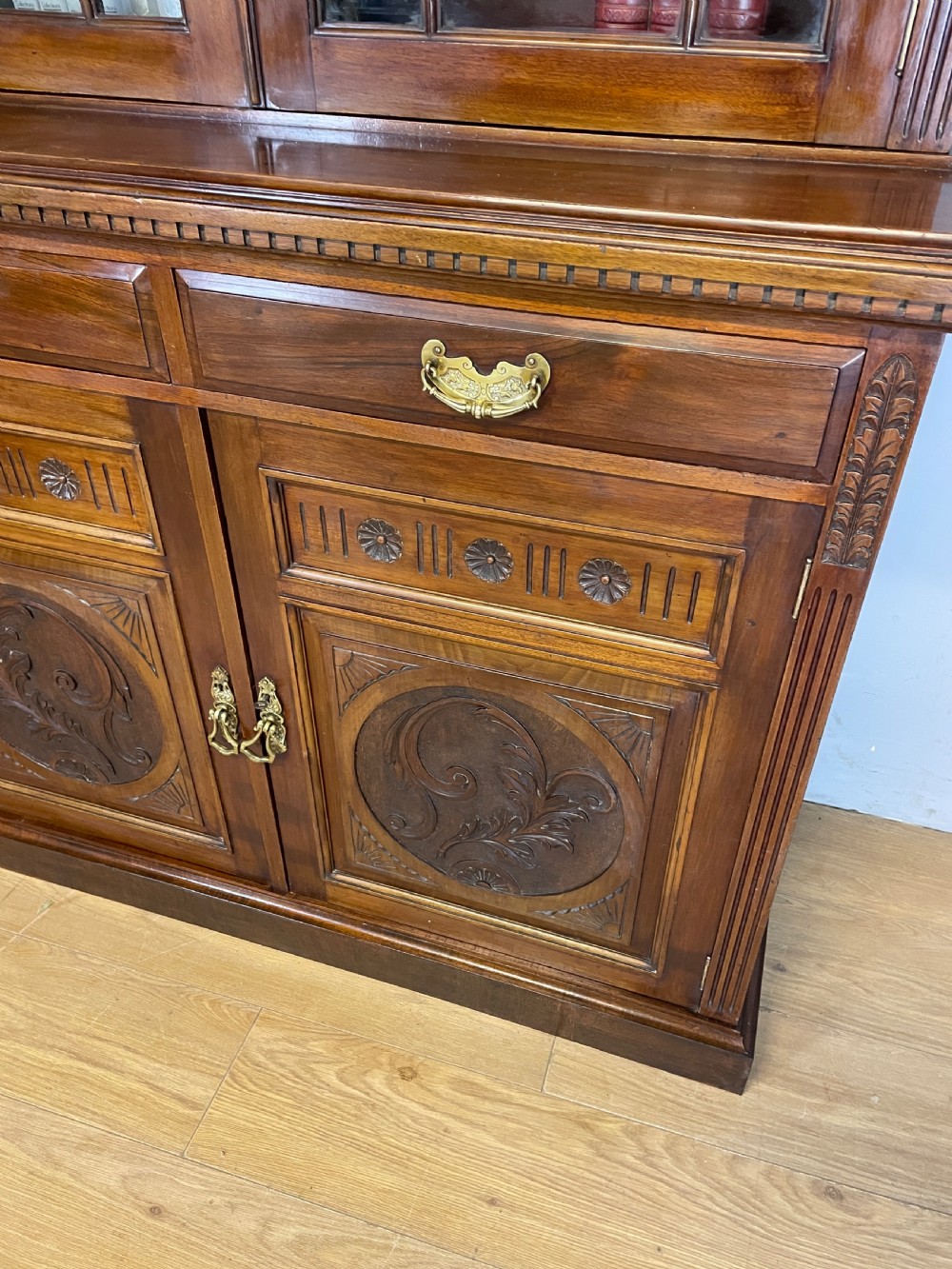 A late 19th-century solid walnut Arts and Crafts bookcase over cupboard featuring upper geometric astragal glazed doors and lower carved foliate panels. View V