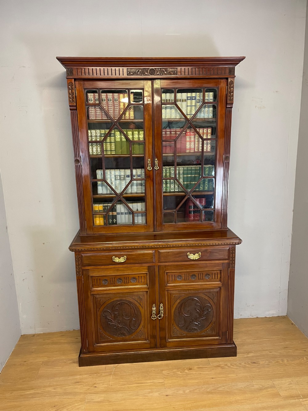 A late 19th-century solid walnut Arts and Crafts bookcase over cupboard featuring upper geometric astragal glazed doors and lower carved foliate panels. View VI