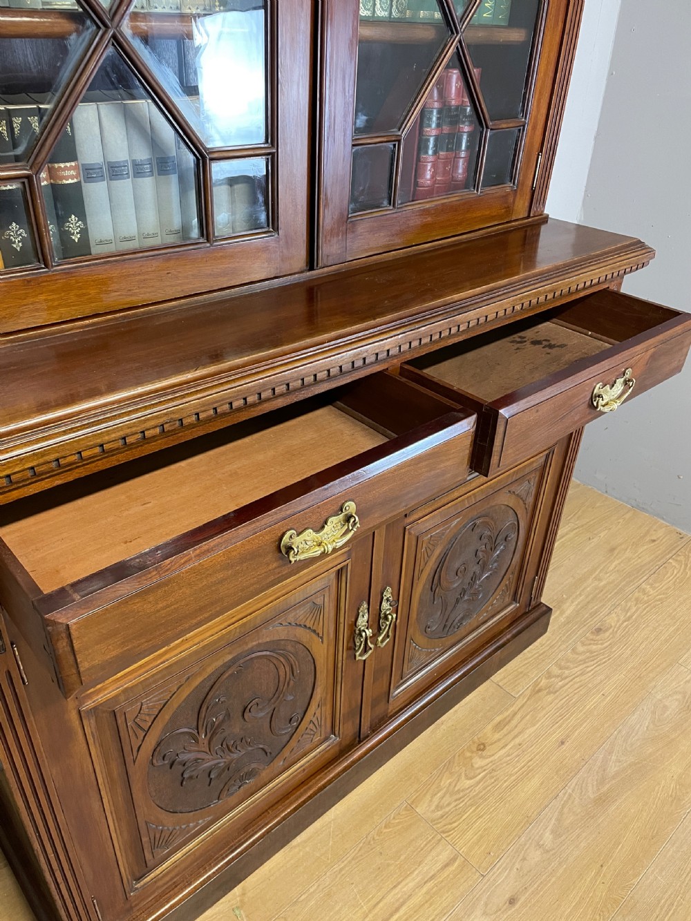 A late 19th-century solid walnut Arts and Crafts bookcase over cupboard featuring upper geometric astragal glazed doors and lower carved foliate panels. View VIII