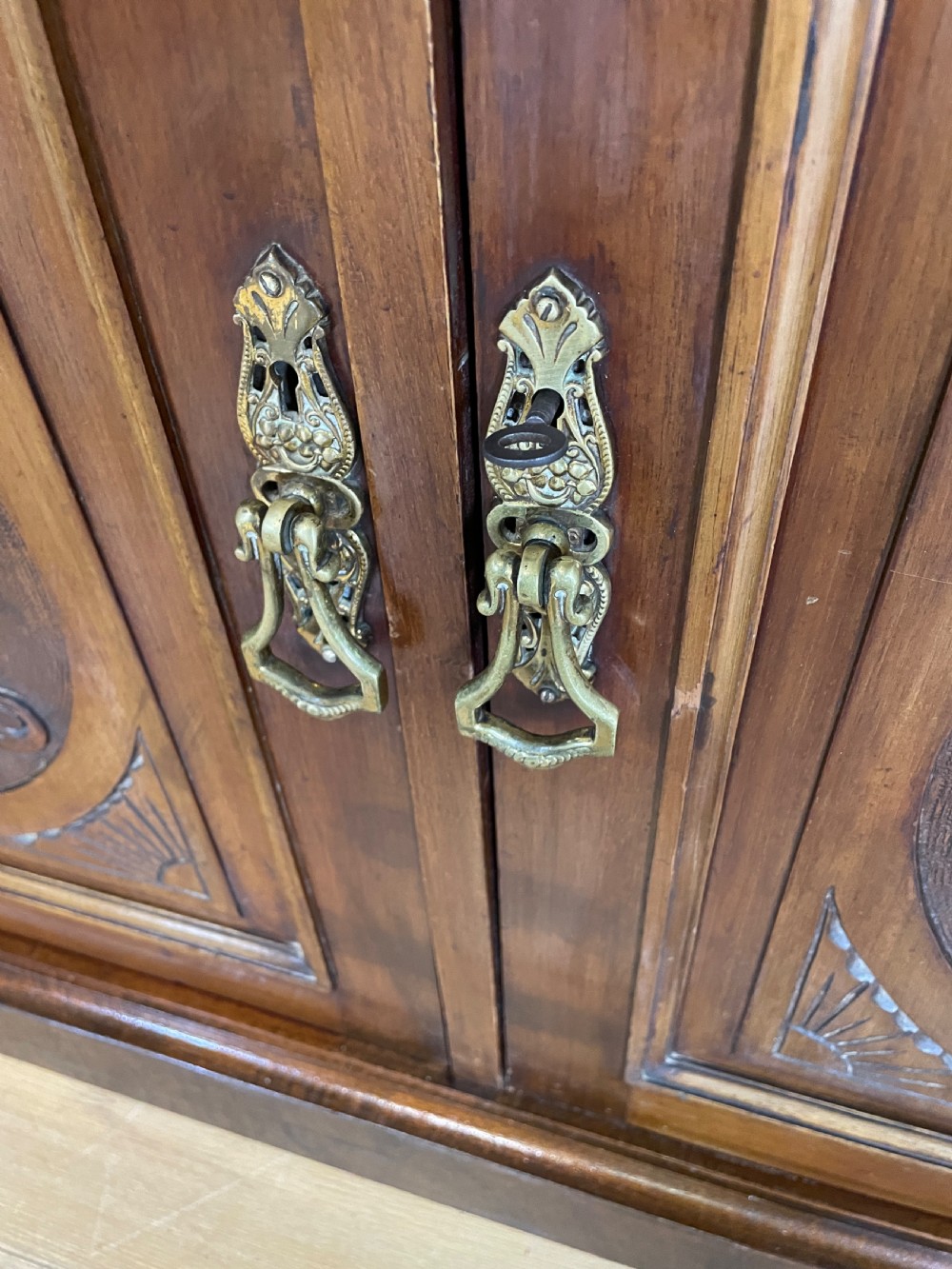 A late 19th-century solid walnut Arts and Crafts bookcase over cupboard featuring upper geometric astragal glazed doors and lower carved foliate panels. View X