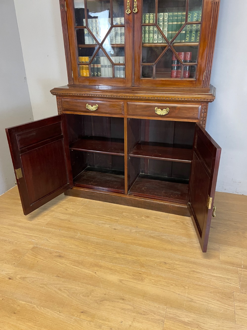 A late 19th-century solid walnut Arts and Crafts bookcase over cupboard featuring upper geometric astragal glazed doors and lower carved foliate panels. View XI