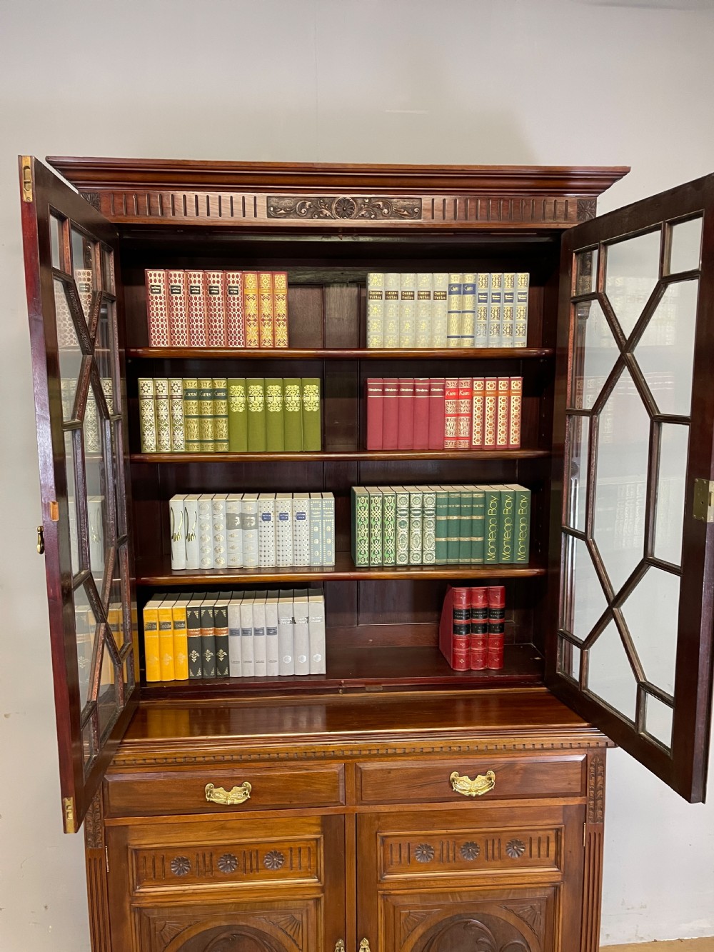 A late 19th-century solid walnut Arts and Crafts bookcase over cupboard featuring upper geometric astragal glazed doors and lower carved foliate panels. View XIII
