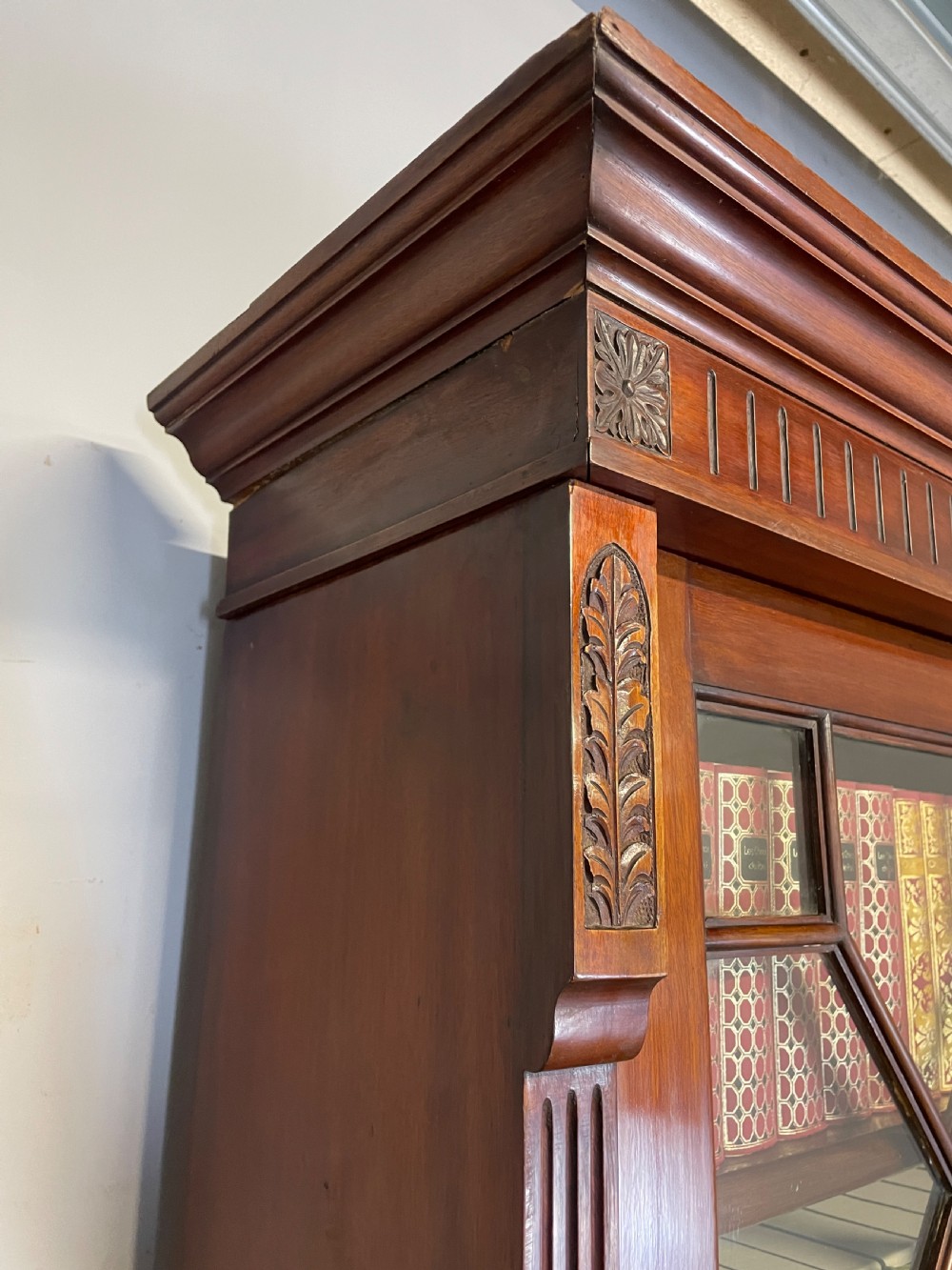 A late 19th-century solid walnut Arts and Crafts bookcase over cupboard featuring upper geometric astragal glazed doors and lower carved foliate panels. View XV