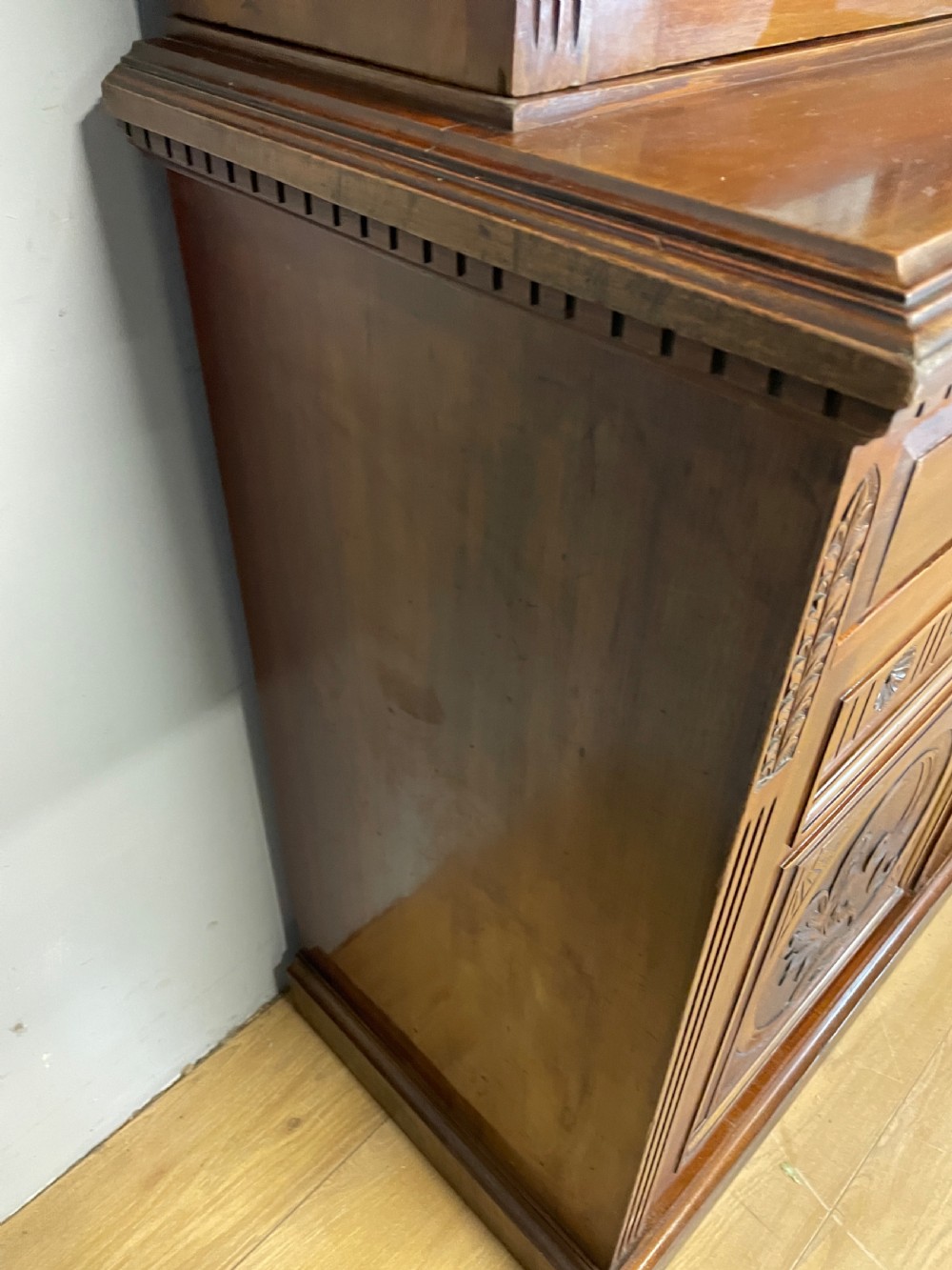 A late 19th-century solid walnut Arts and Crafts bookcase over cupboard featuring upper geometric astragal glazed doors and lower carved foliate panels. View XVI