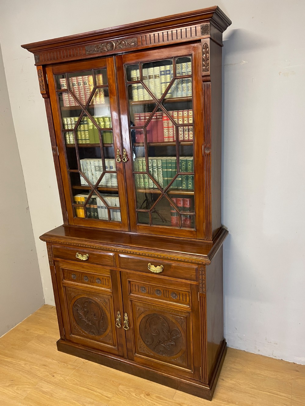 A late 19th-century solid walnut Arts and Crafts bookcase over cupboard featuring upper geometric astragal glazed doors and lower carved foliate panels. View XVII