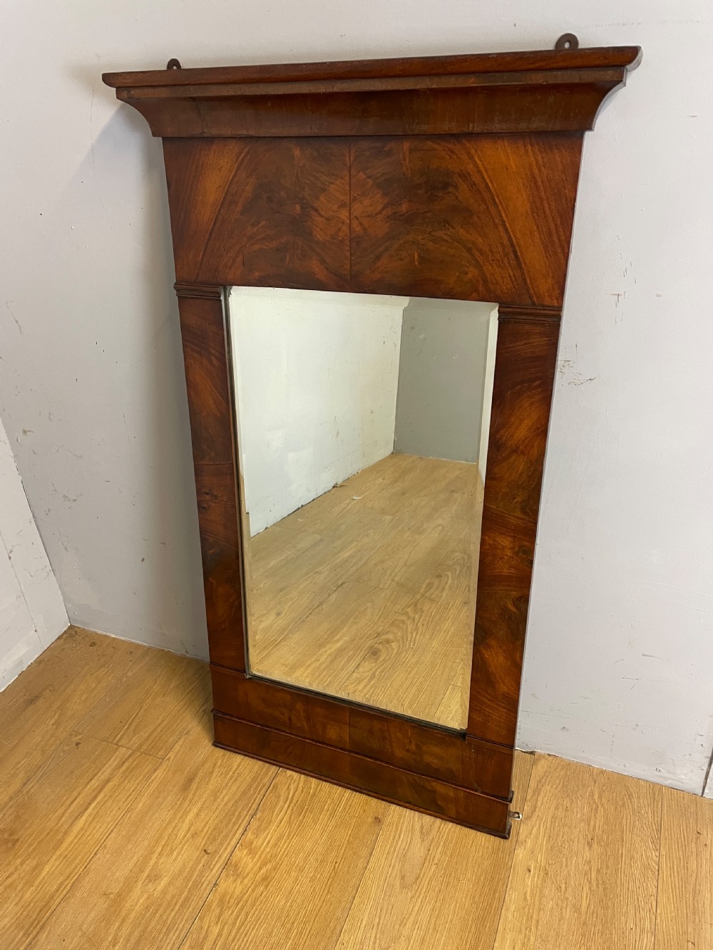 A nineteenth-century Biedermeier rectangular wall mirror featuring book-matched flame mahogany veneers and a stepped architectural top moulding.