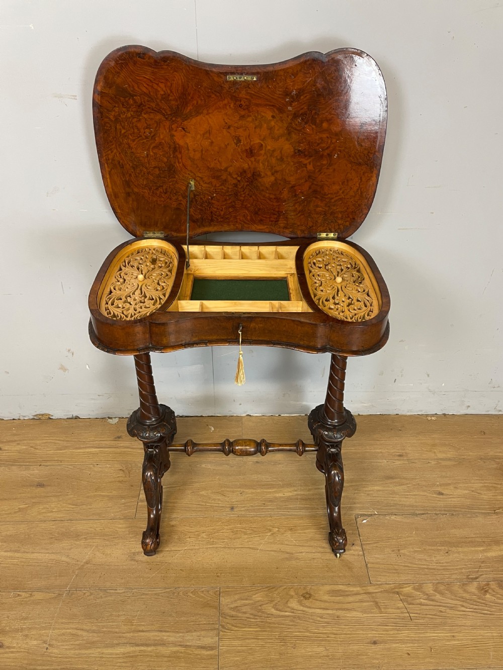 A Victorian burr walnut work table shown with its hinged lid open, revealing intricate fretwork covers, internal compartments, and carved turned legs. View III
