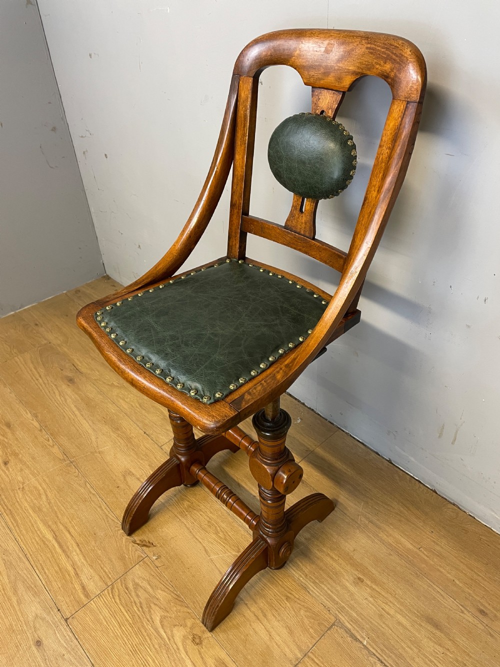 A late nineteenth-century Victorian patent music chair in polished oak featuring a green leather seat and lumbar pad trimmed with brass studs.