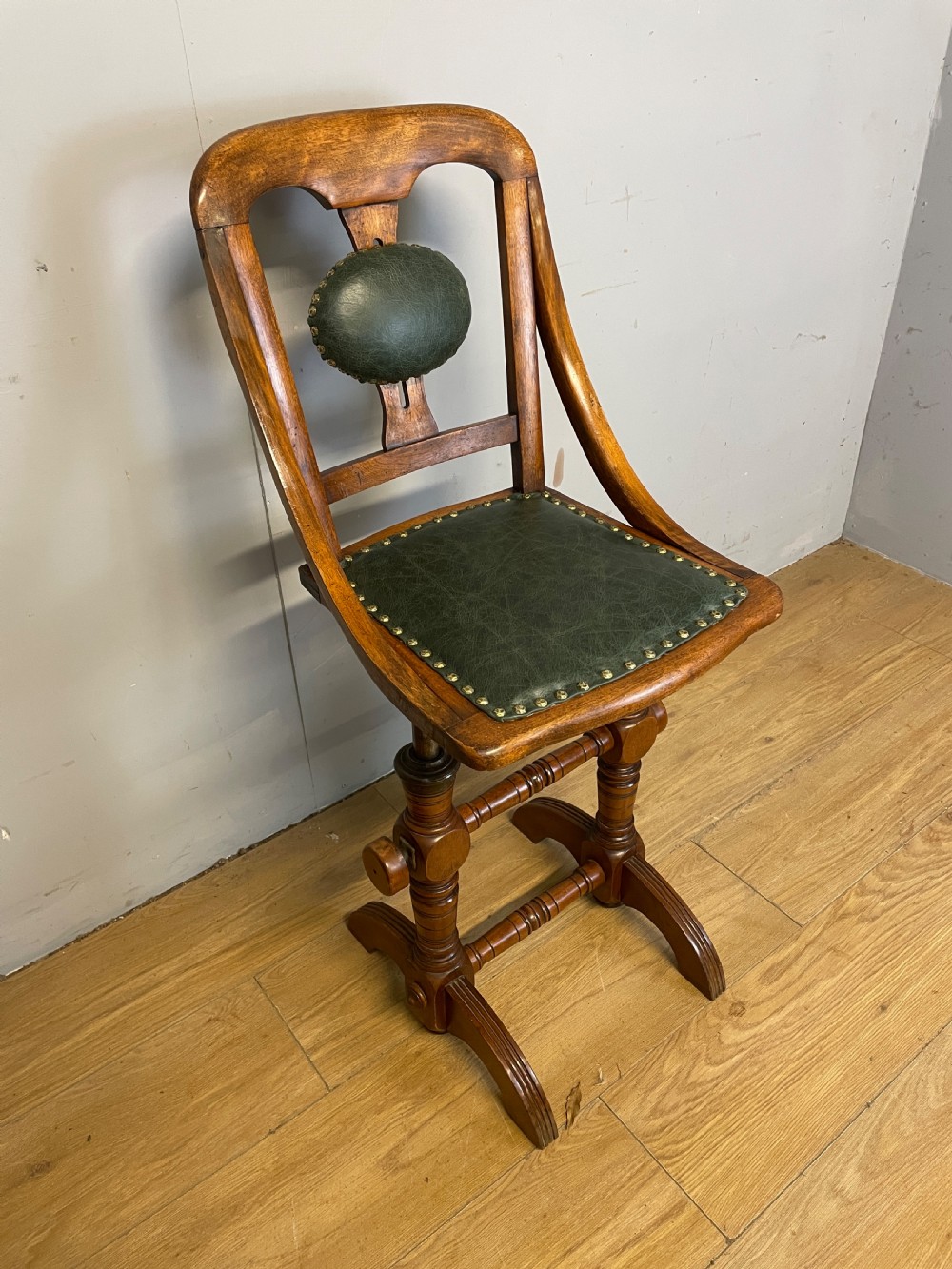 A late nineteenth-century Victorian patent music chair in polished oak featuring a green leather seat and lumbar pad trimmed with brass studs. View II