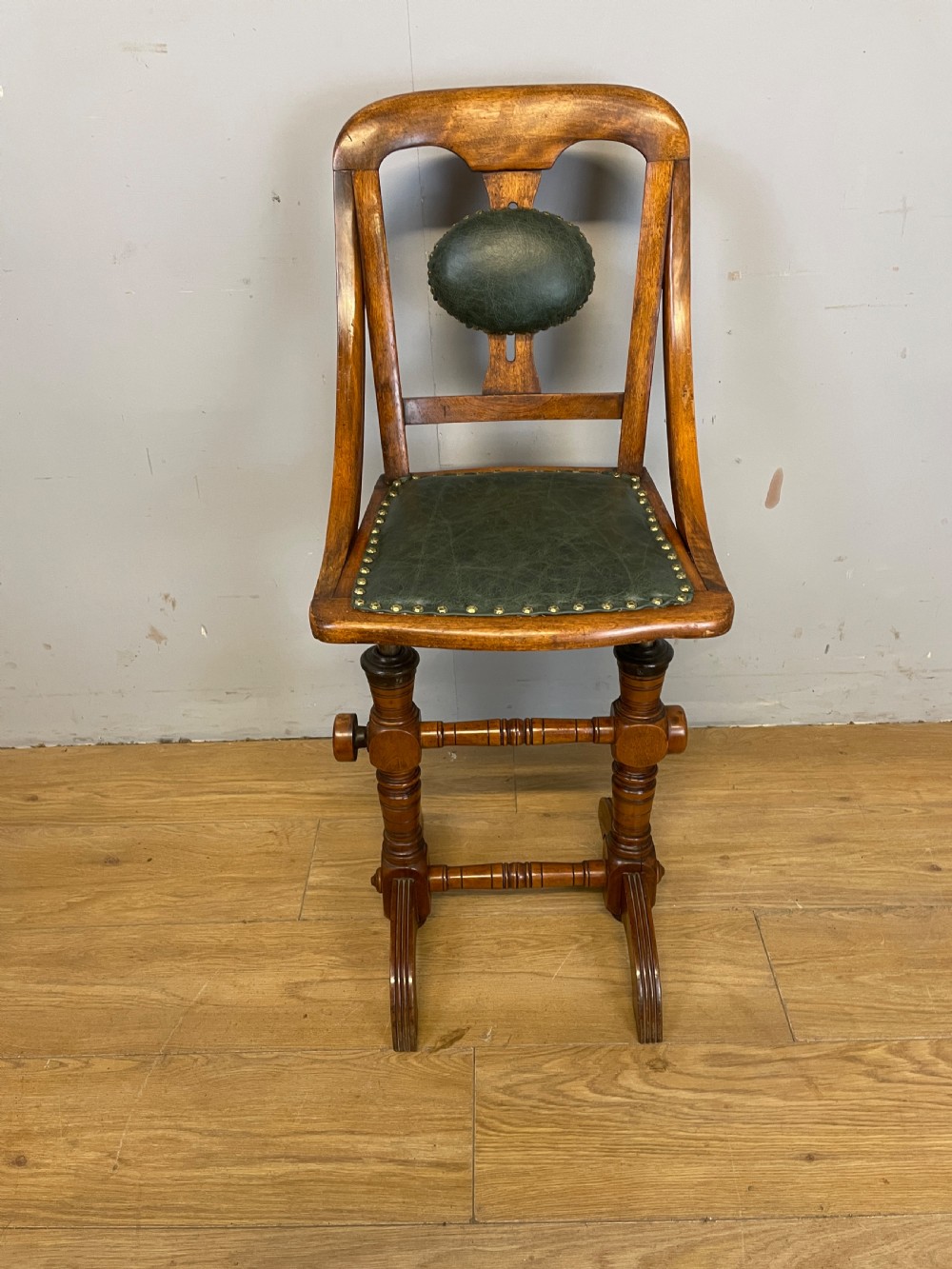 A late nineteenth-century Victorian patent music chair in polished oak featuring a green leather seat and lumbar pad trimmed with brass studs. View III