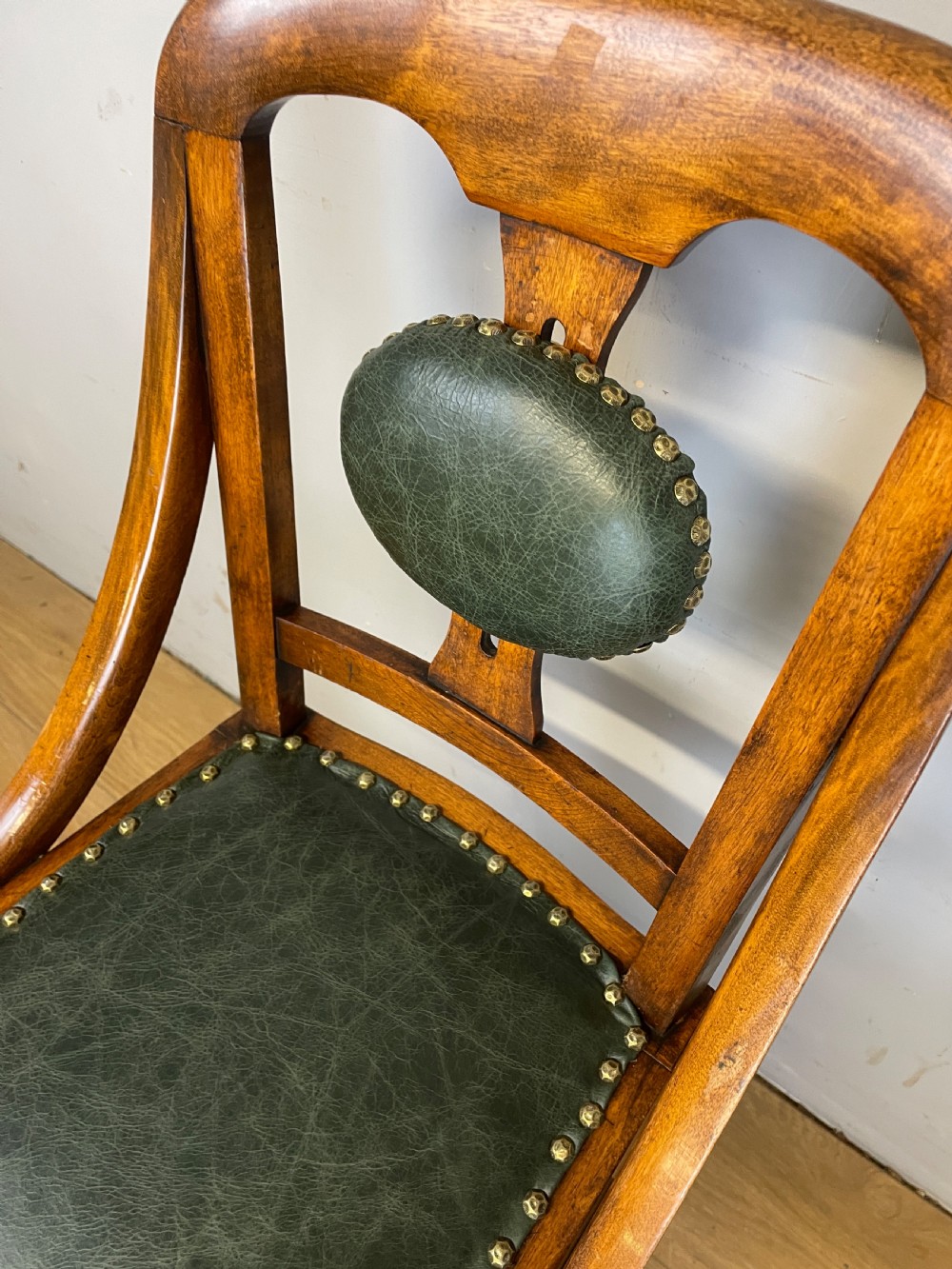 A late nineteenth-century Victorian patent music chair in polished oak featuring a green leather seat and lumbar pad trimmed with brass studs. View V