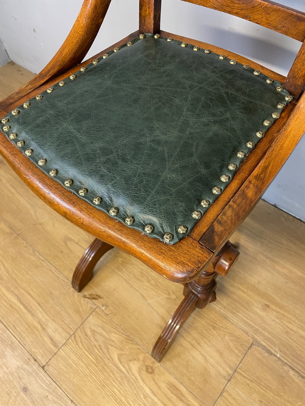A late nineteenth-century Victorian patent music chair in polished oak featuring a green leather seat and lumbar pad trimmed with brass studs. View VI
