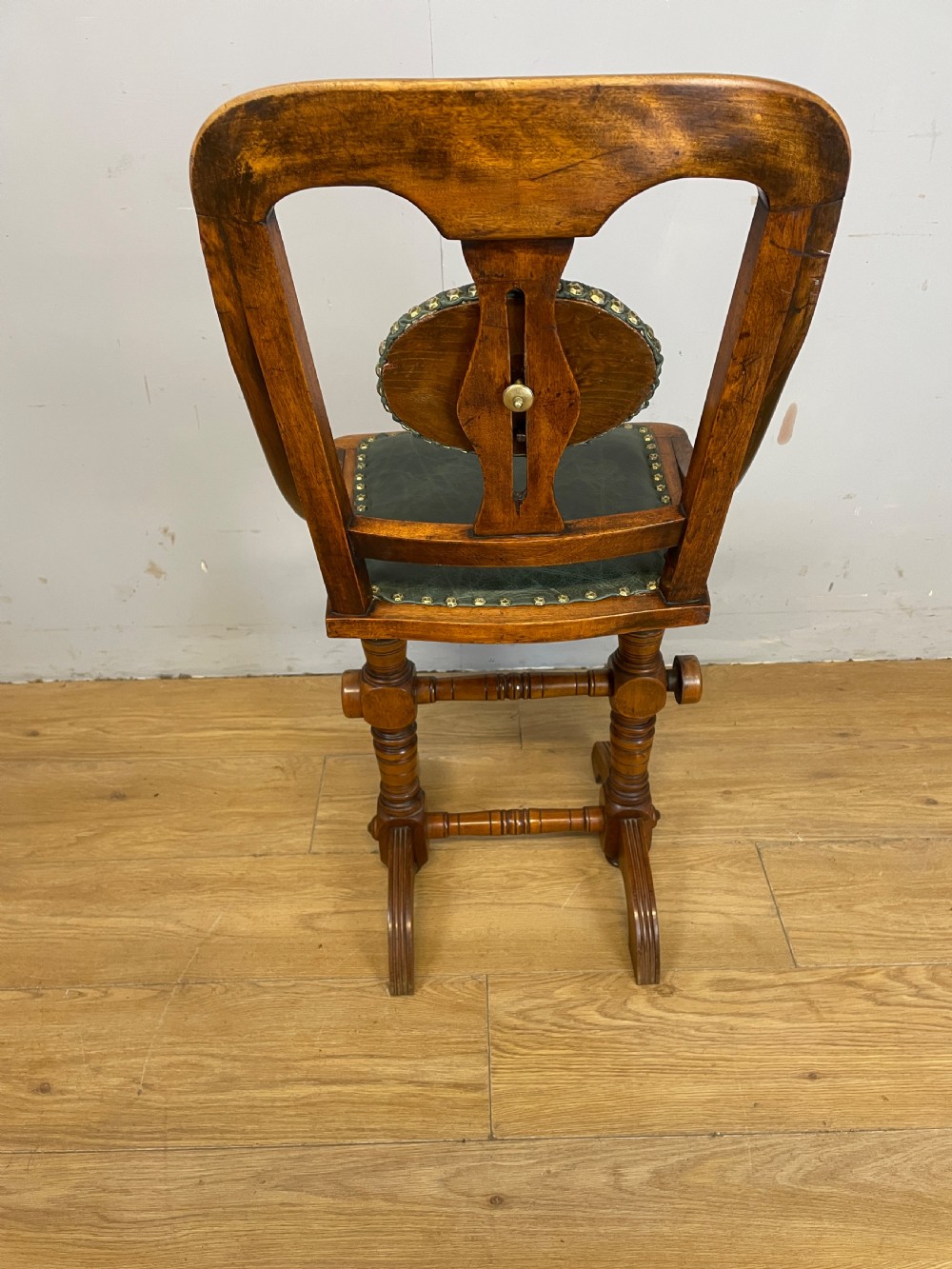 A late nineteenth-century Victorian patent music chair in polished oak featuring a green leather seat and lumbar pad trimmed with brass studs. View VII