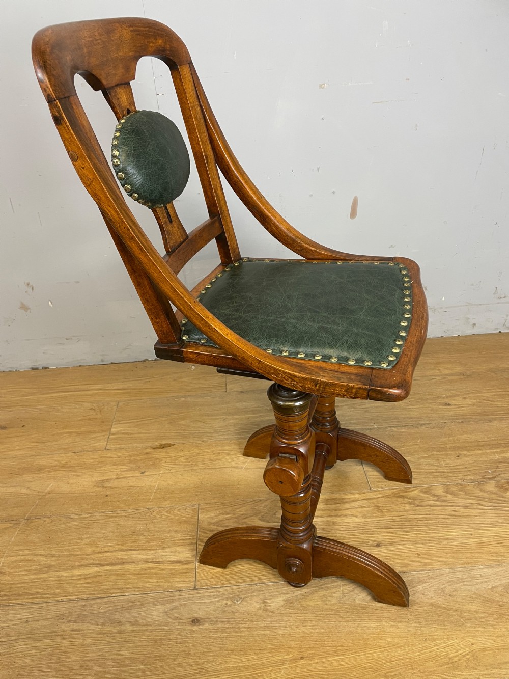 A late nineteenth-century Victorian patent music chair in polished oak featuring a green leather seat and lumbar pad trimmed with brass studs. View XII