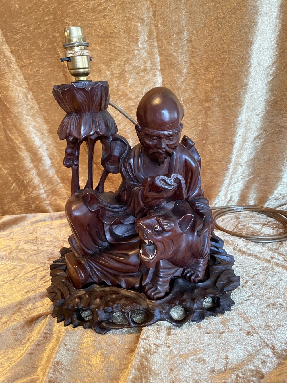 Late nineteenth-century Chinese carved dark wood table lamp depicting a seated scholar figure reading beside a tiger on a carved base with brass bulb holder.