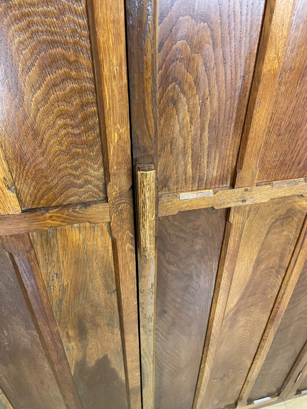 A solid warm brown oak wardrobe featuring vertical panelled double doors and exposed wooden handles in the Cotswold School style. View IV
