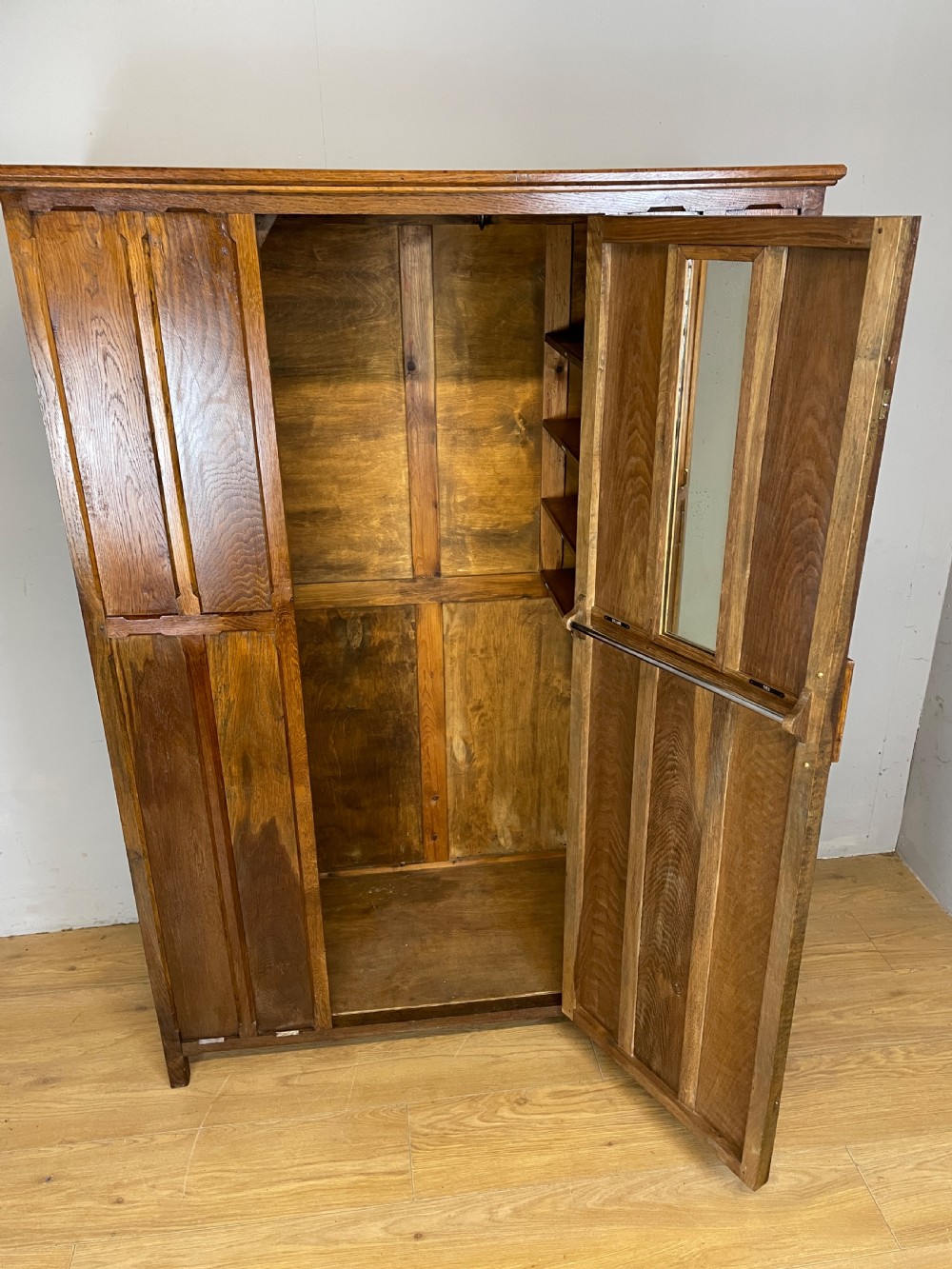 A solid warm brown oak wardrobe featuring vertical panelled double doors and exposed wooden handles in the Cotswold School style. View V