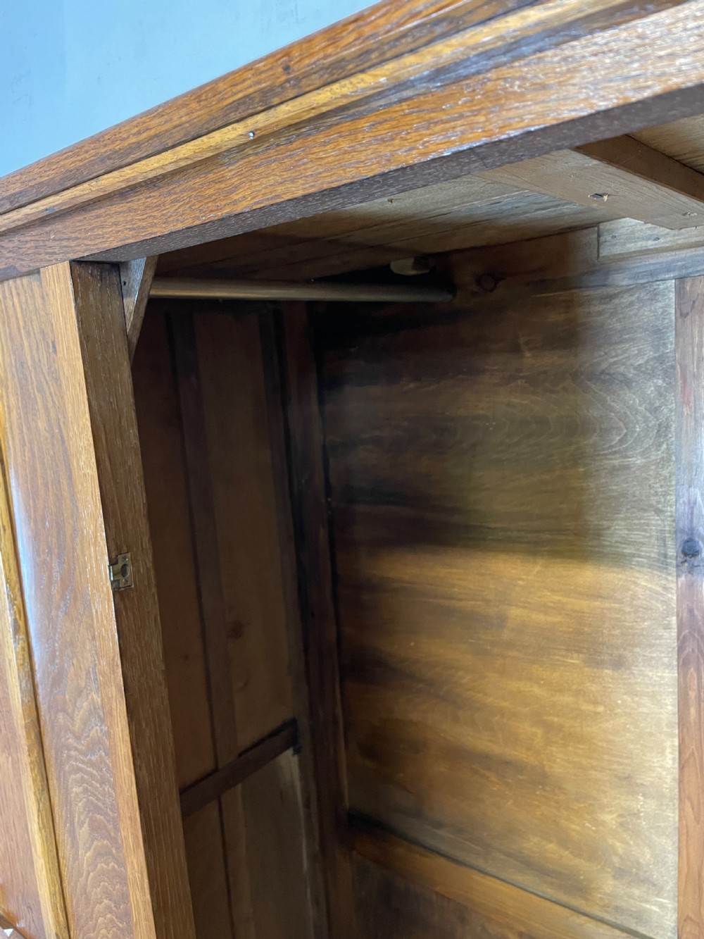 A solid warm brown oak wardrobe featuring vertical panelled double doors and exposed wooden handles in the Cotswold School style. View VIII