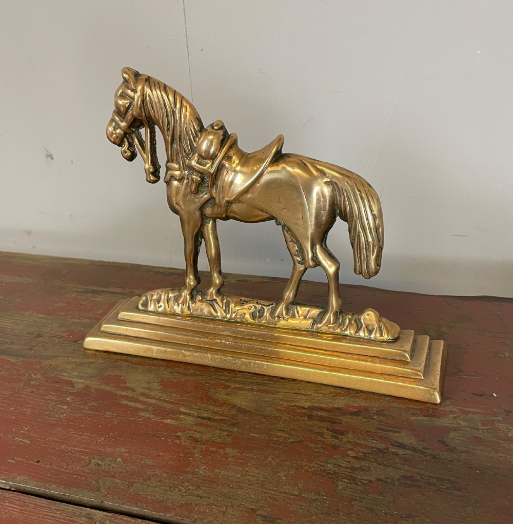 A 19th-century cast brass doorstop featuring a detailed saddled horse standing on a stepped rectangular base.