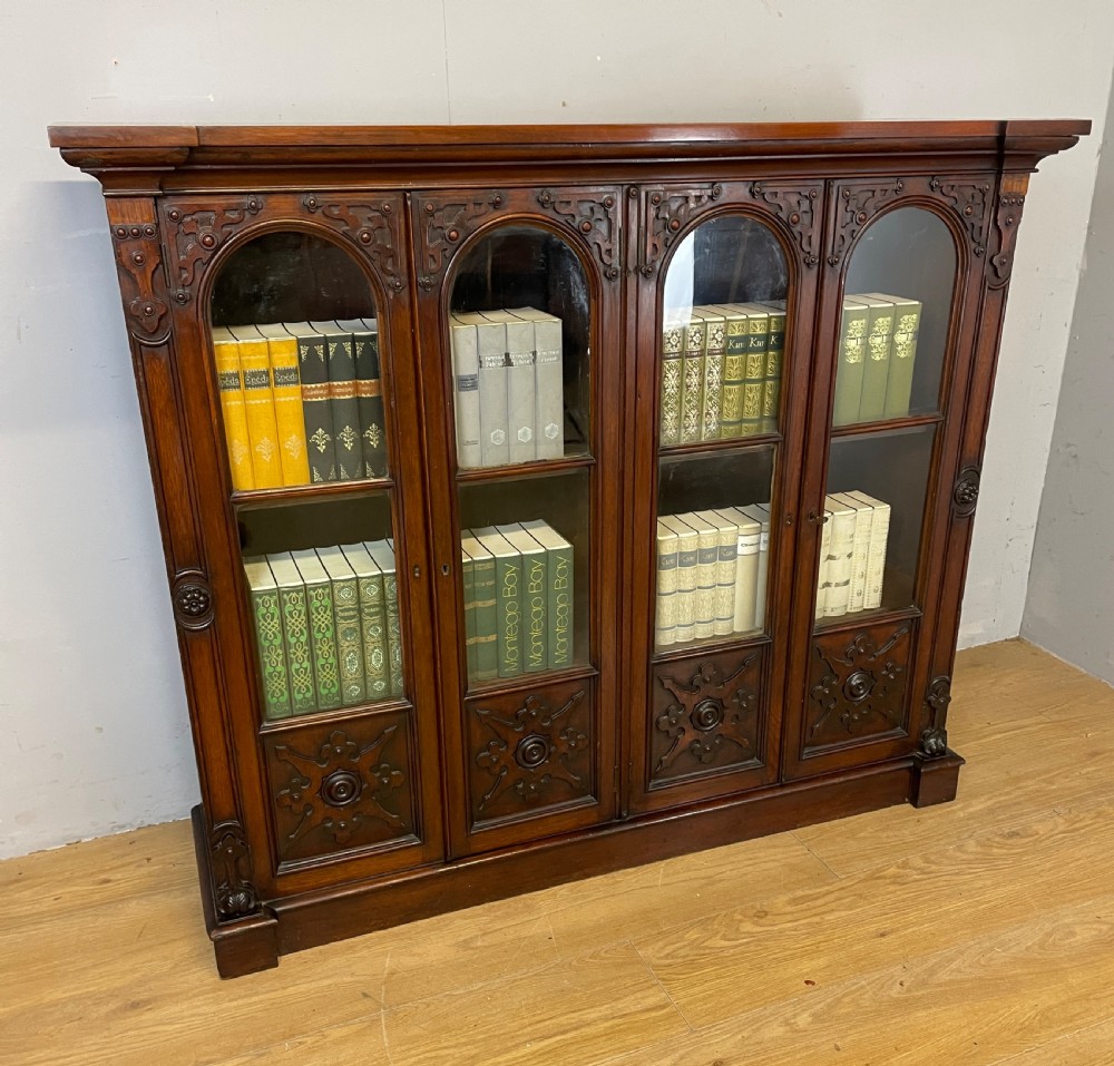 A nineteenth-century walnut low bookcase featuring four arched glazed doors with carved Gothic Revival panel detailing.