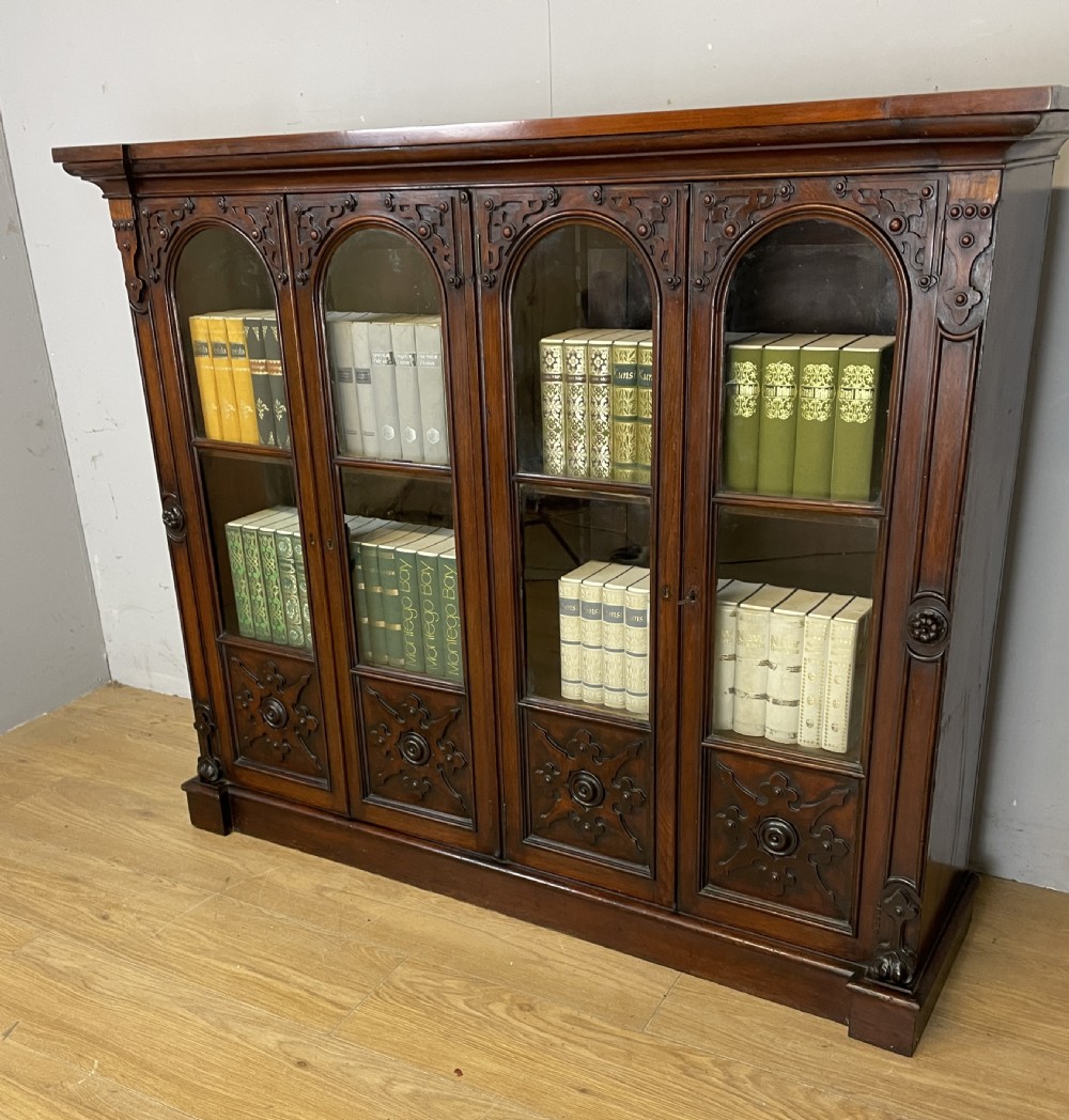 A nineteenth-century walnut low bookcase featuring four arched glazed doors with carved Gothic Revival panel detailing. View II